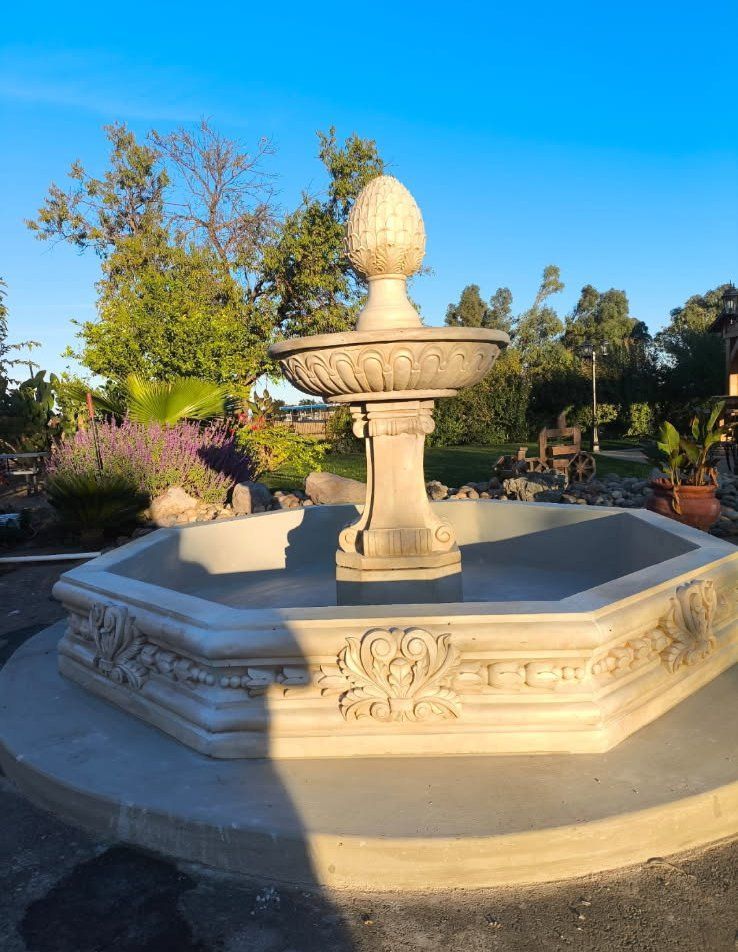 Stone fountain in a landscaped garden under a clear blue sky.