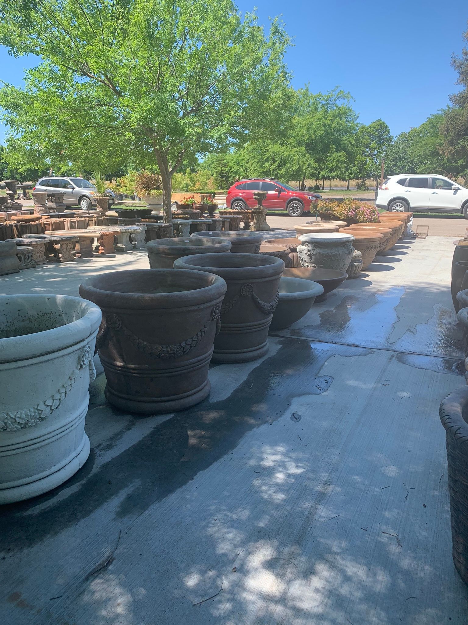Outdoor plant nursery with rows of large decorative planters in sunlit gravel lot