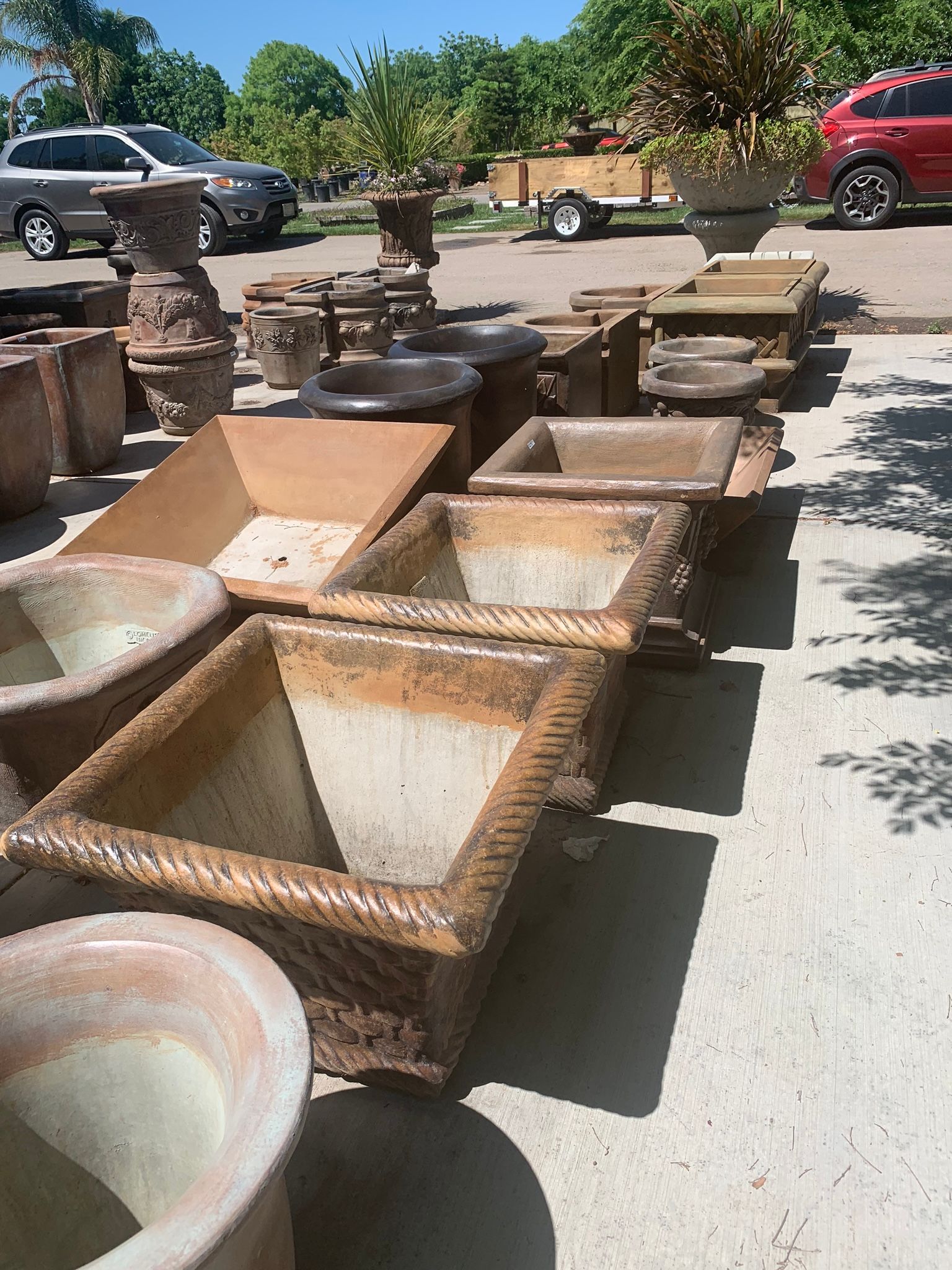 Outdoor display of large stone and ceramic planters in various shapes and colors on a sunny patio
