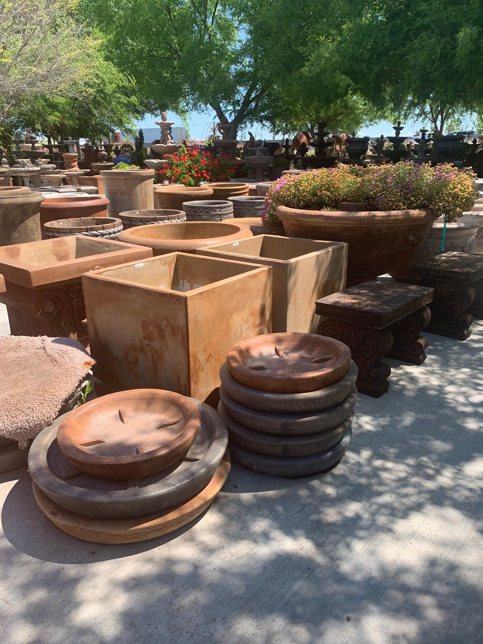Outdoor display of stacked stone garden planters and pots under trees in bright sunlight