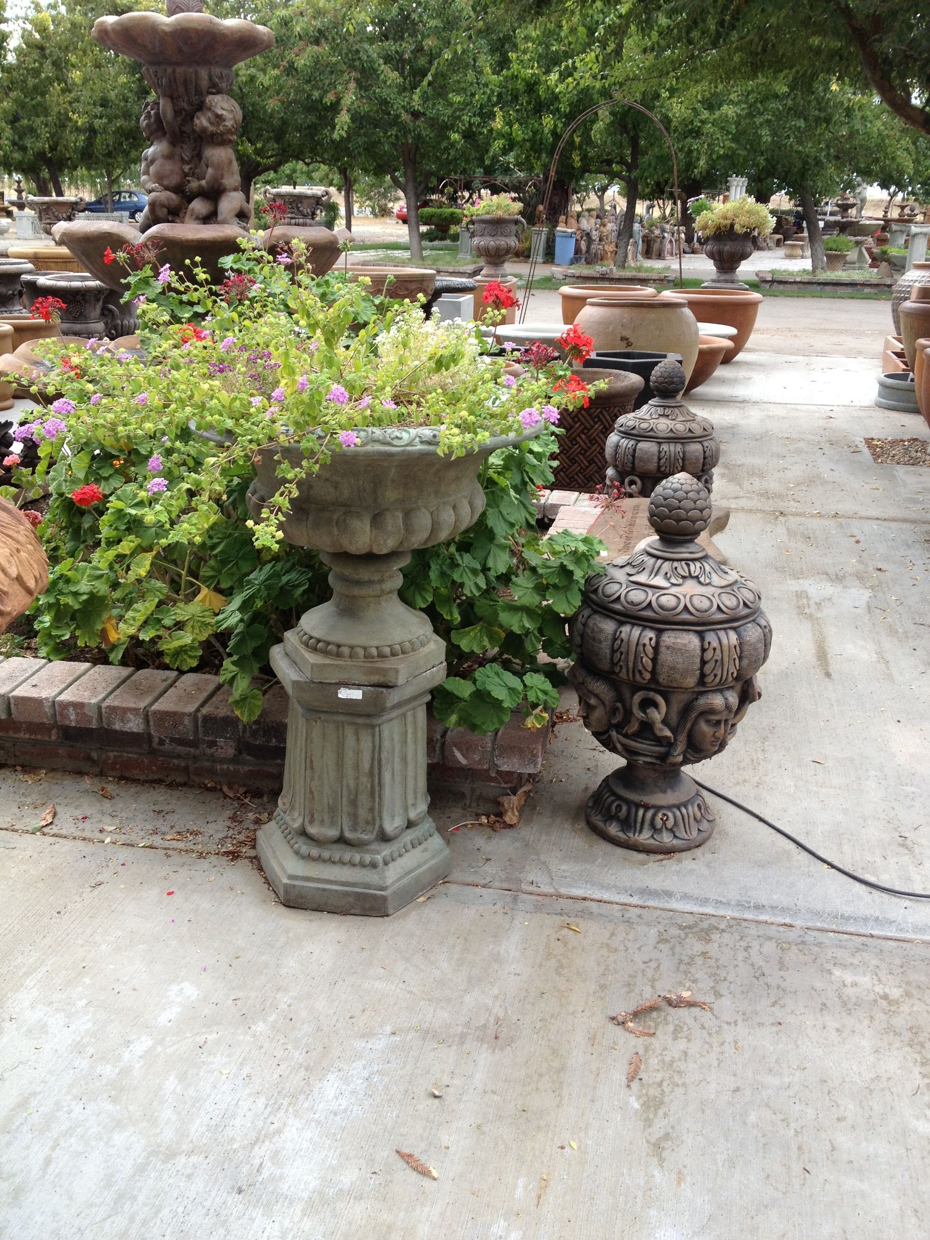 Garden walkway with decorative stone urns and flowers under green trees