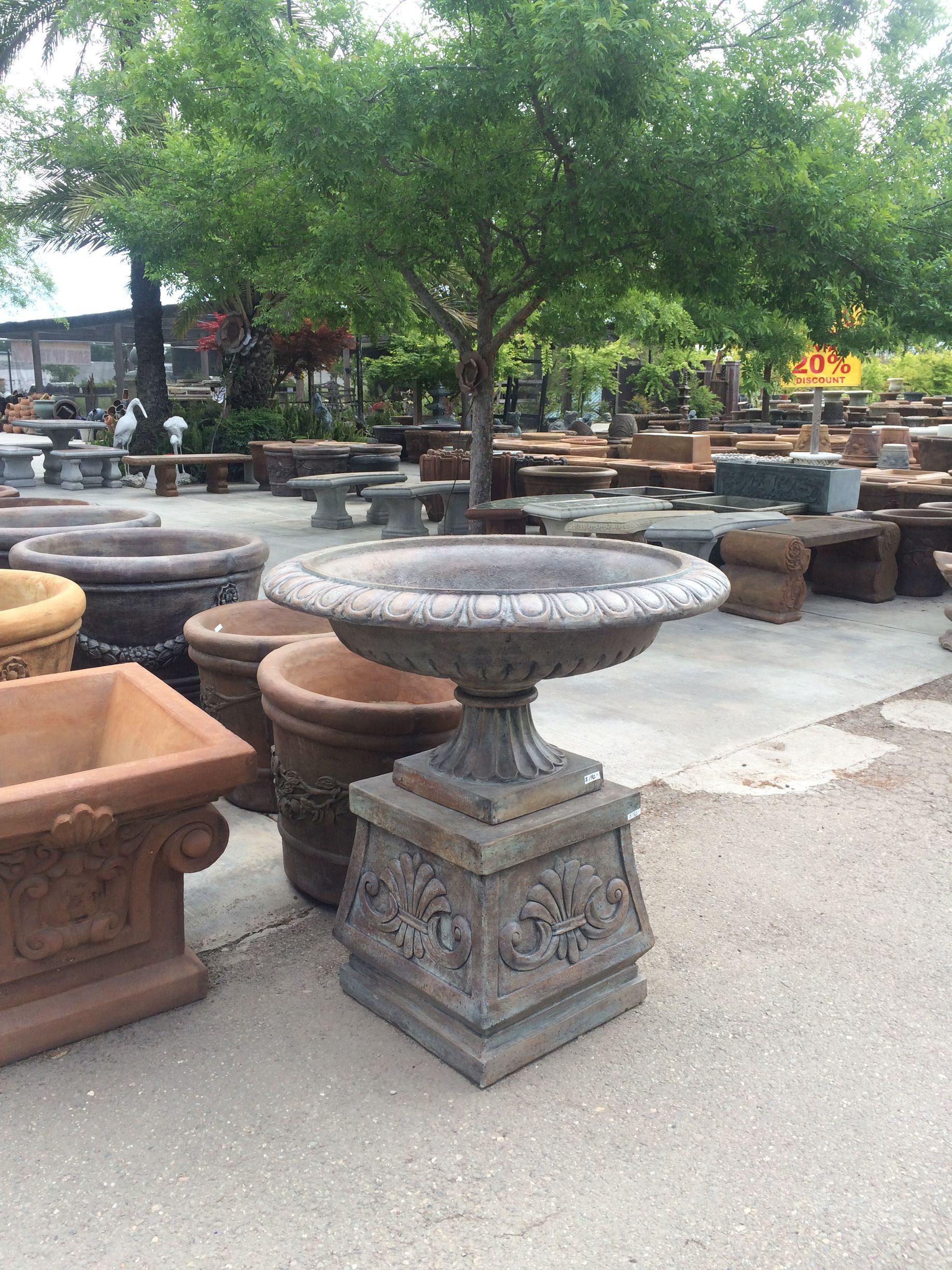 Outdoor garden center with decorative stone planters and fountains under a leafy tree