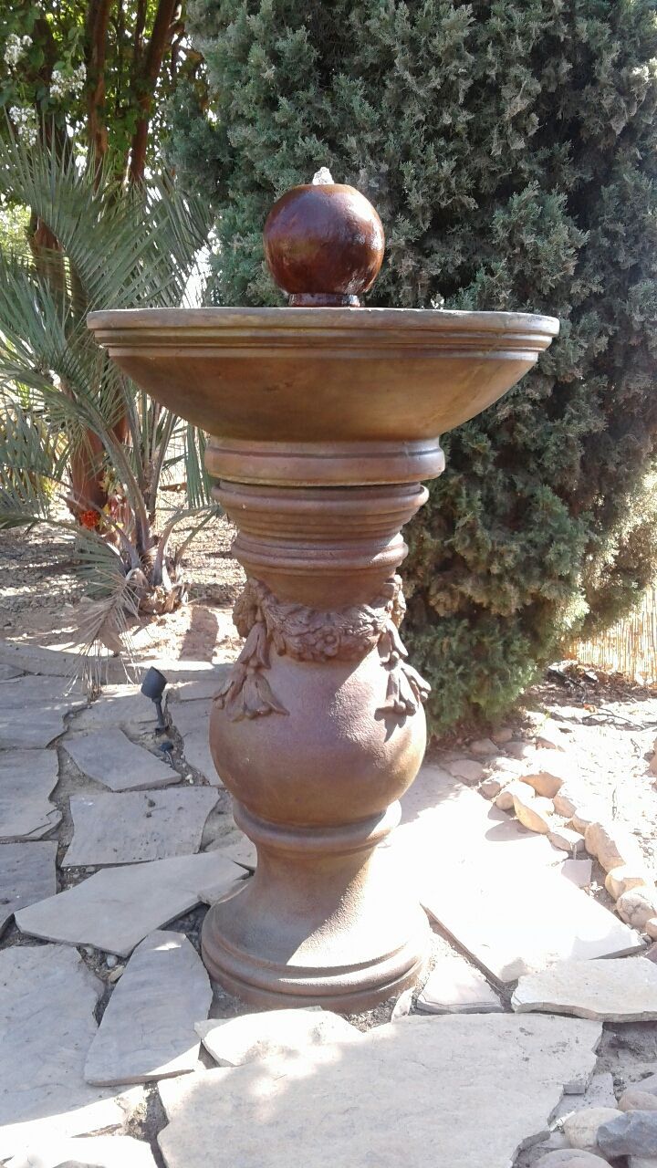 Decorative stone pedestal urn with a round finial in a sunlit garden path