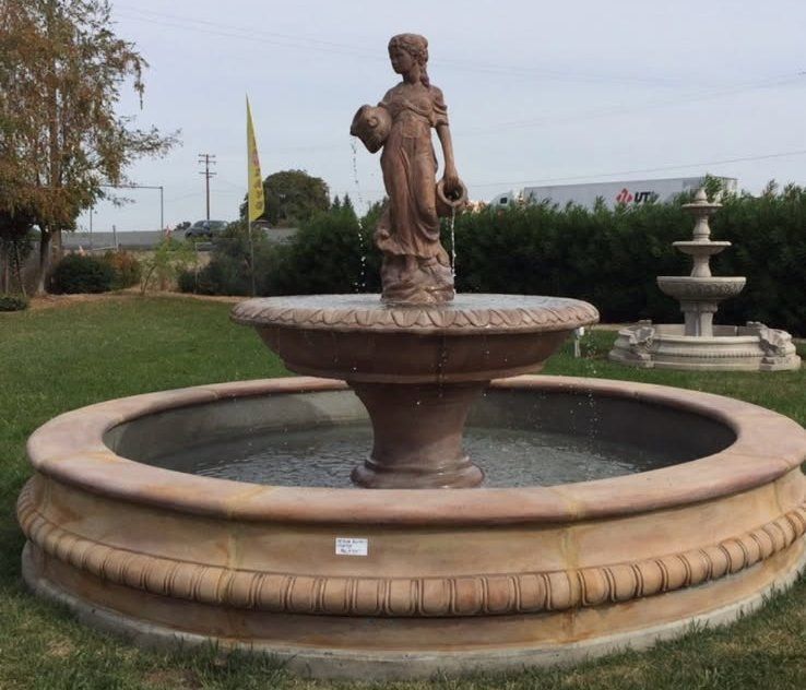 Outdoor stone fountain with a statue in the center and a smaller fountain in the background
