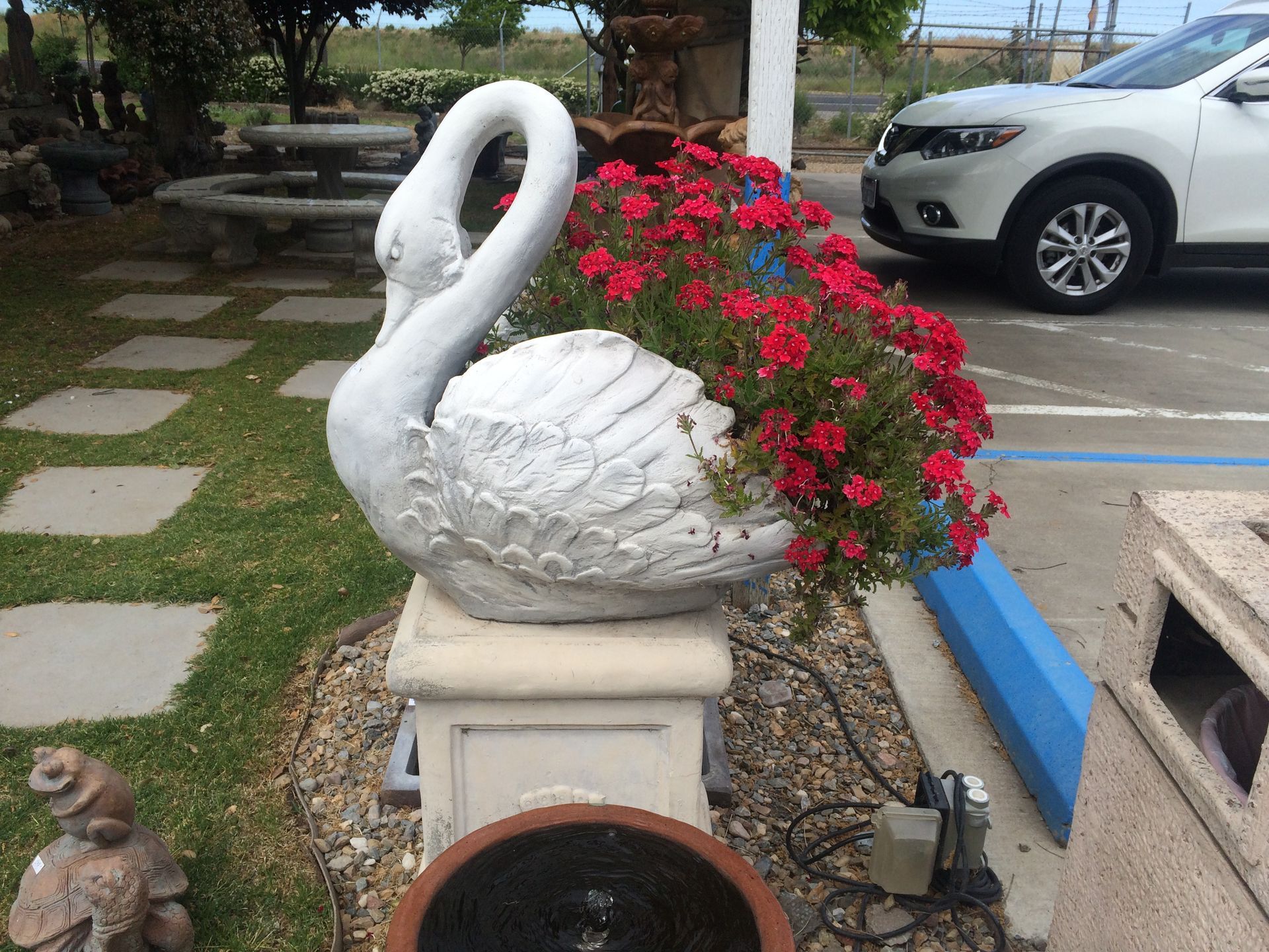White swan planter with red flowers beside a parking lot and stone path