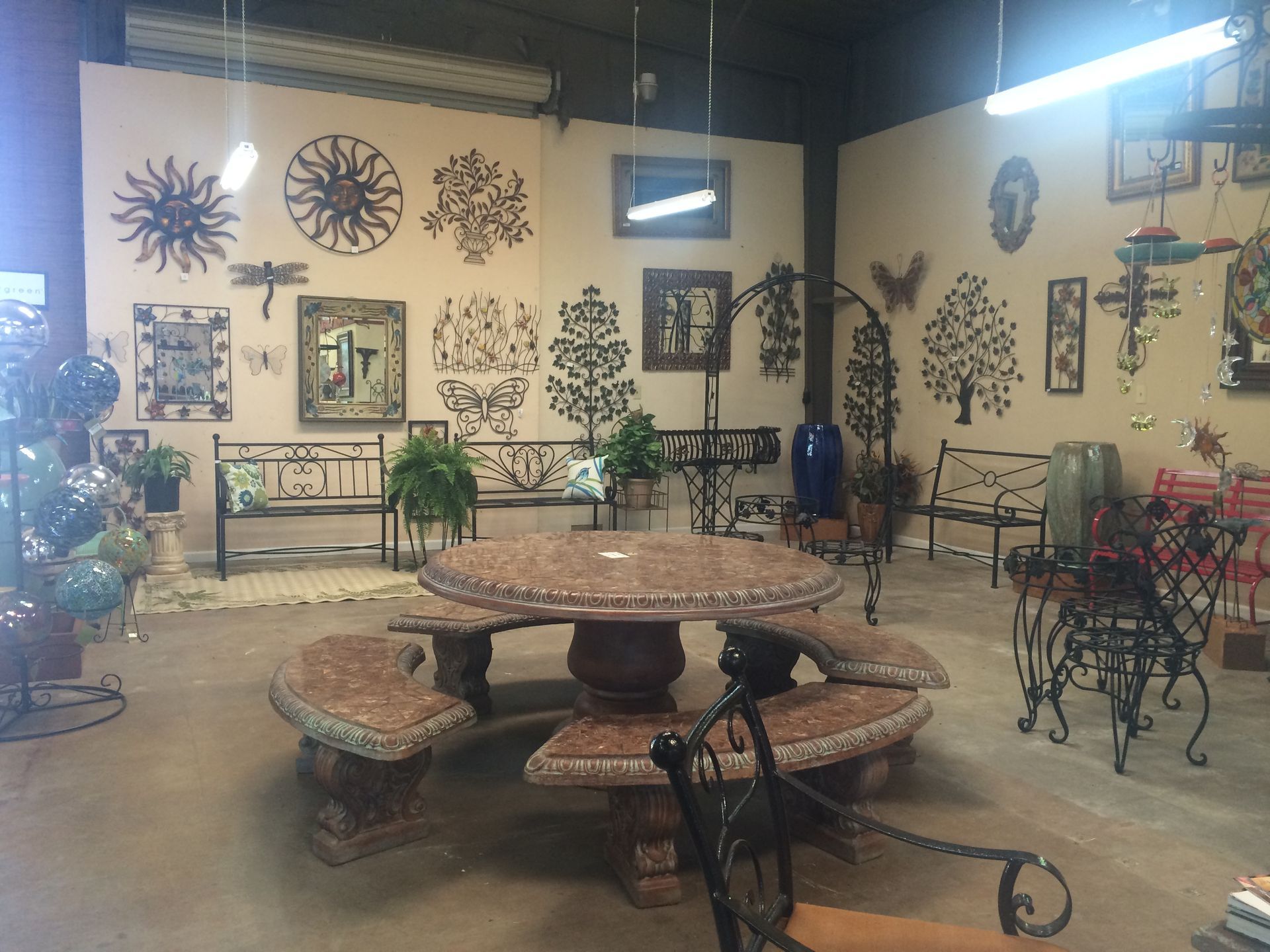 Indoor showroom with wrought-iron patio furniture, metal wall art, and decorative tables on a concrete floor