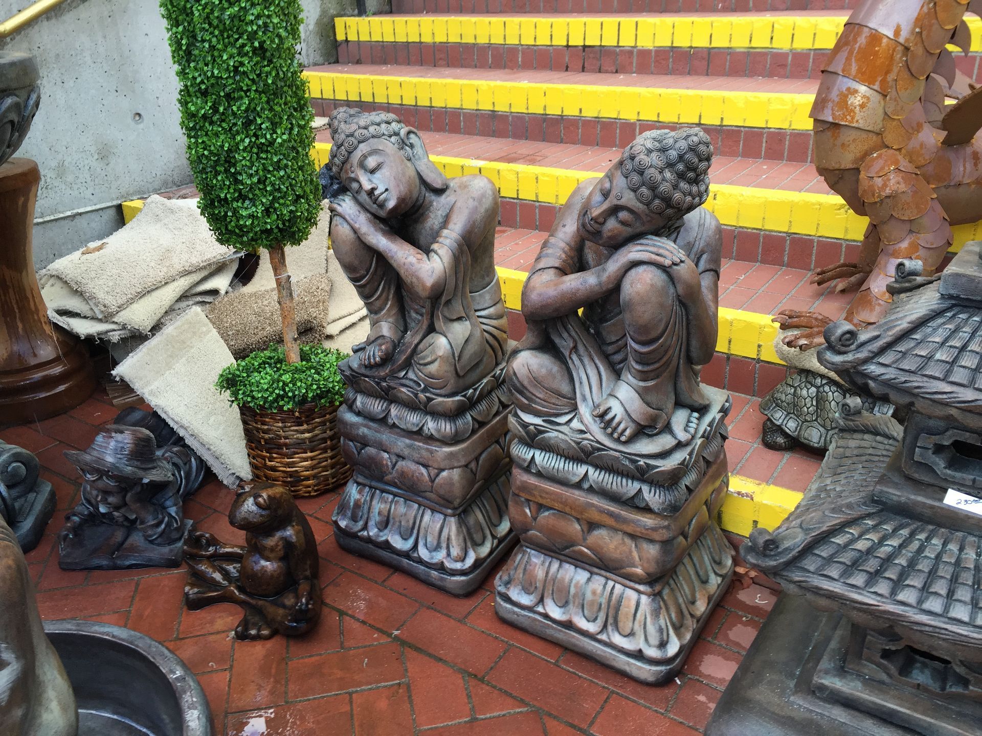 Small stone figurines on a tiled stairway beside yellow-and-red steps and a potted topiary
