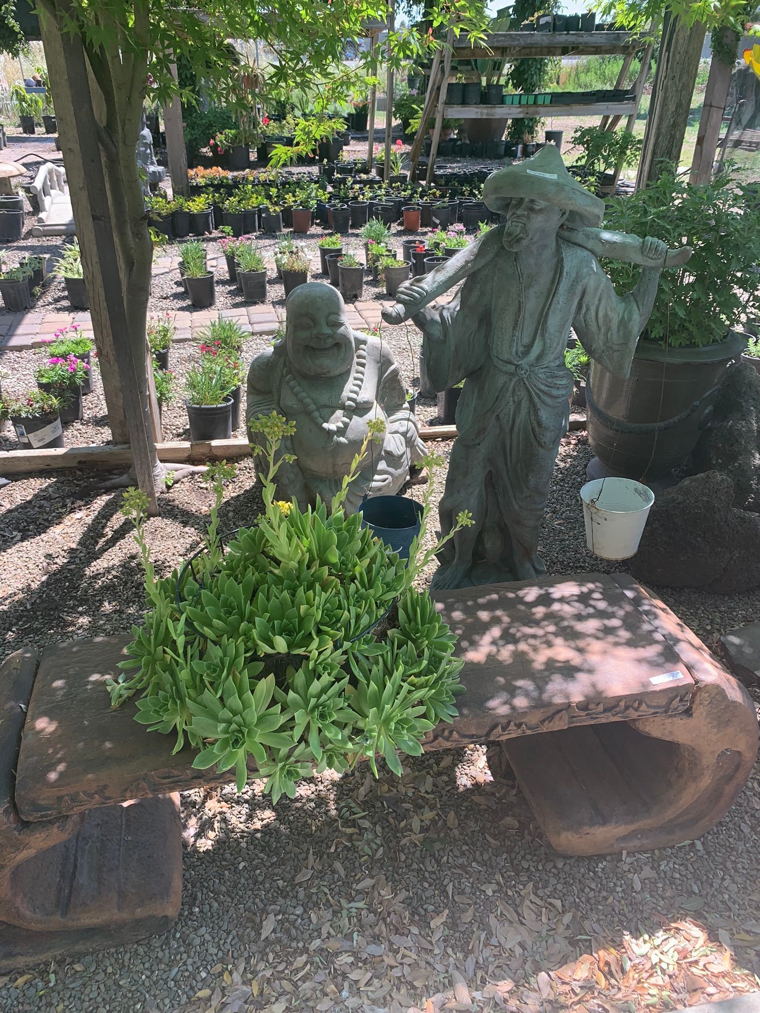 Small outdoor garden with stone statues, potted plants, and greenery among rocks and brick edging