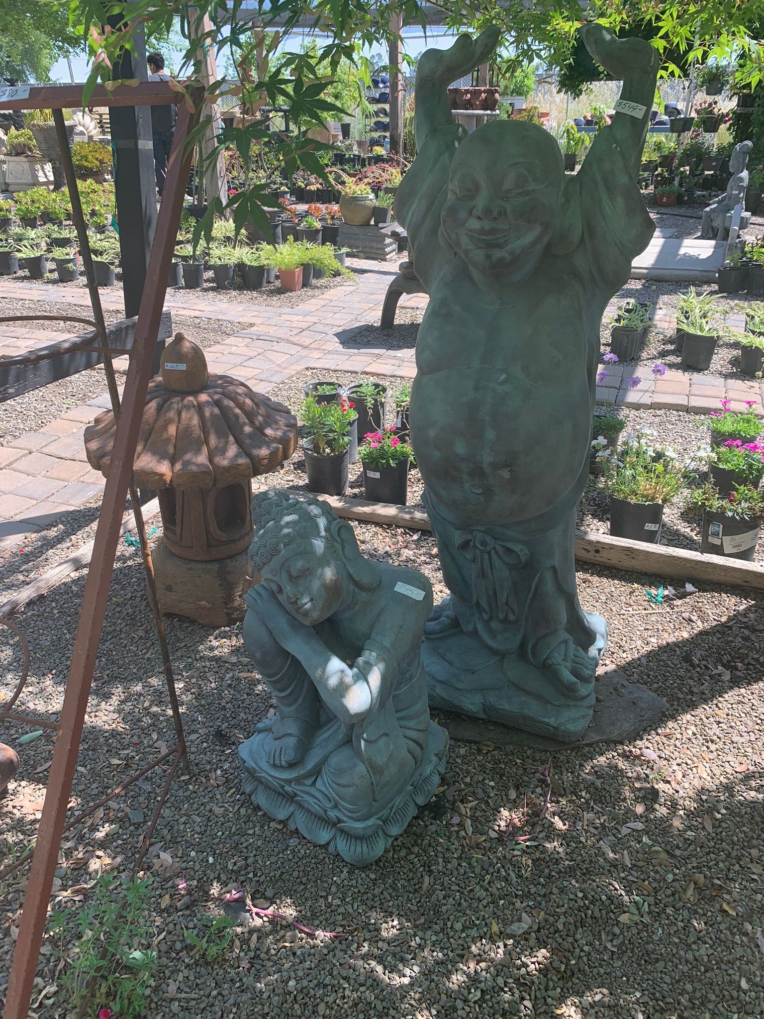 Garden display of weathered stone statues and potted plants in a sunny outdoor nursery