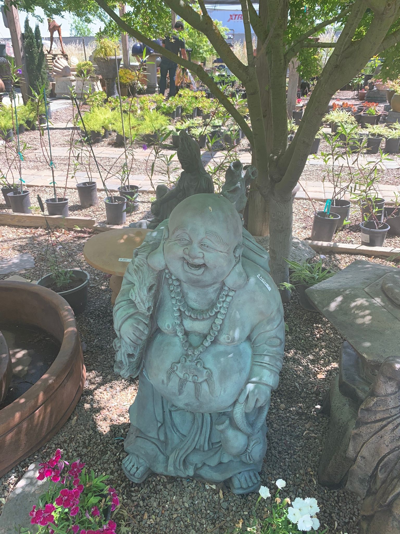 Stone Buddha statue among flowers in a garden, beside a tree and rustic pots