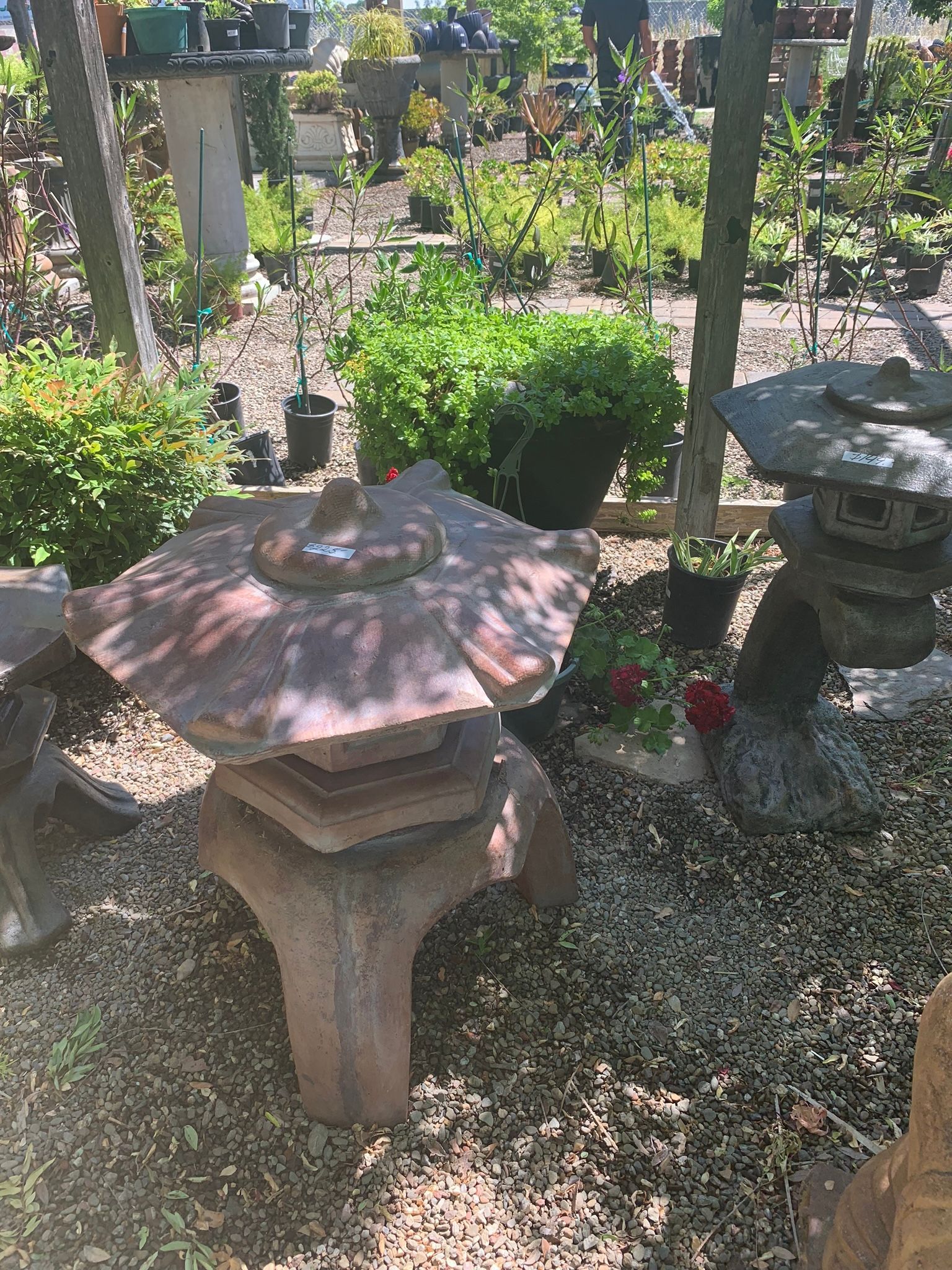Stone garden lantern among gravel, potted greenery, and dappled sunlight in a landscaped garden