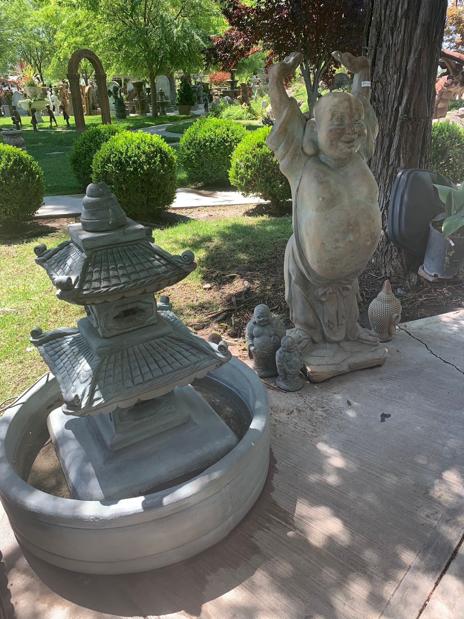 Stone pagoda fountain beside a cat statue in a shaded garden