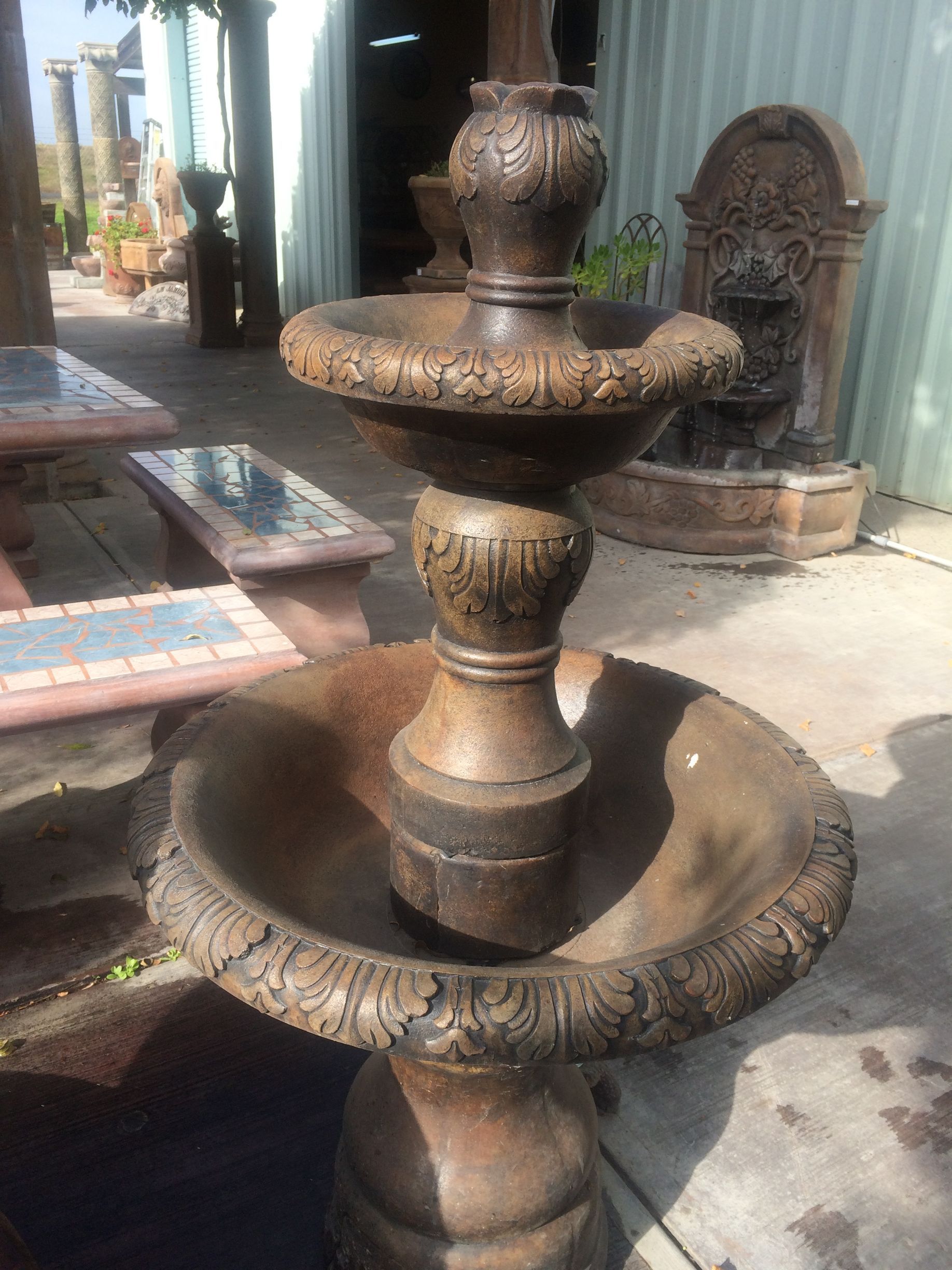 Three-tiered stone fountain in a courtyard, with weathered brown basins and a decorative back wall.