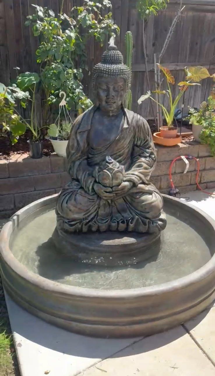 Buddha statue seated in a shallow round water basin in a garden patio