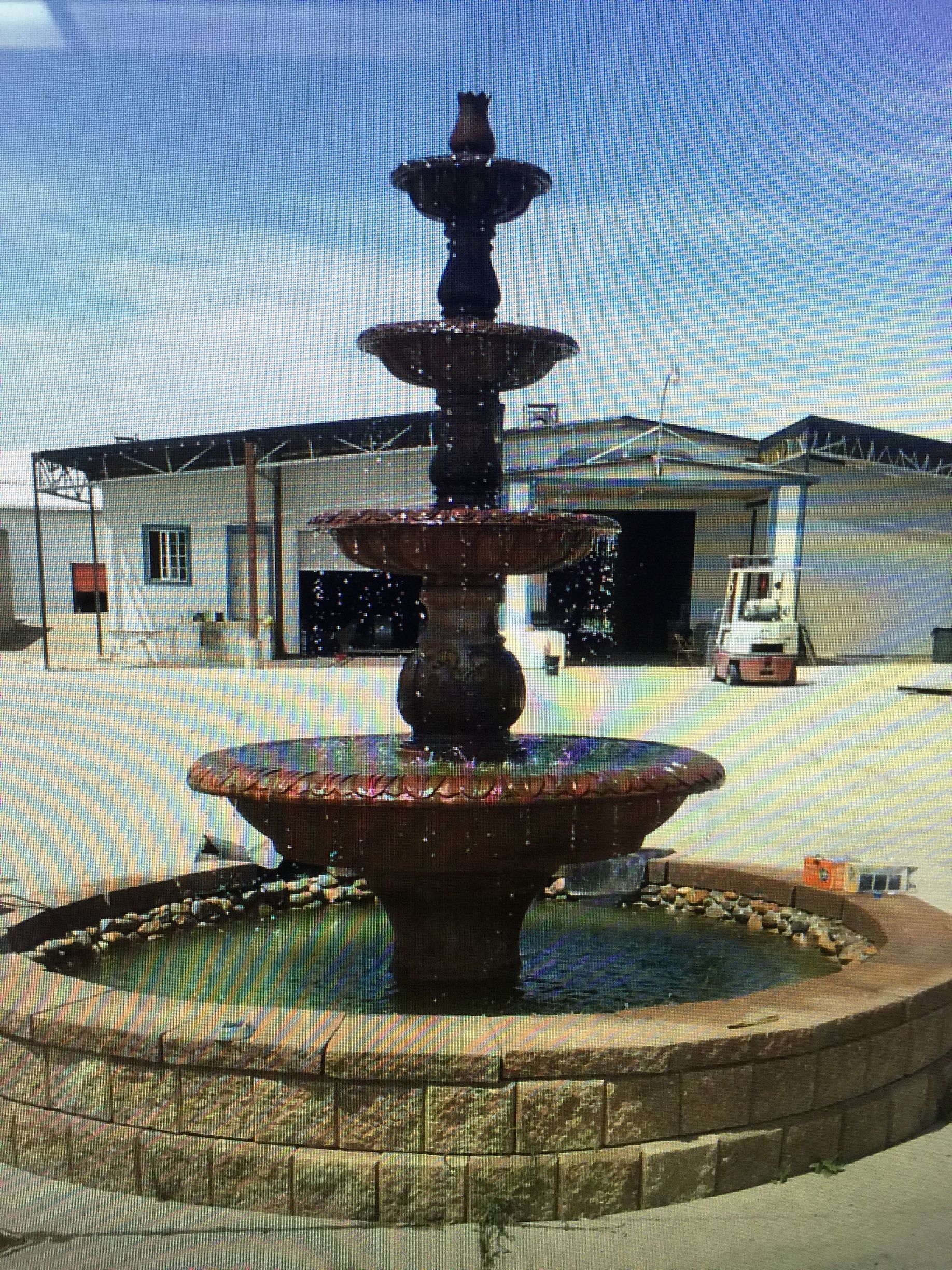 Tiered stone fountain in a courtyard, with buildings in the background.