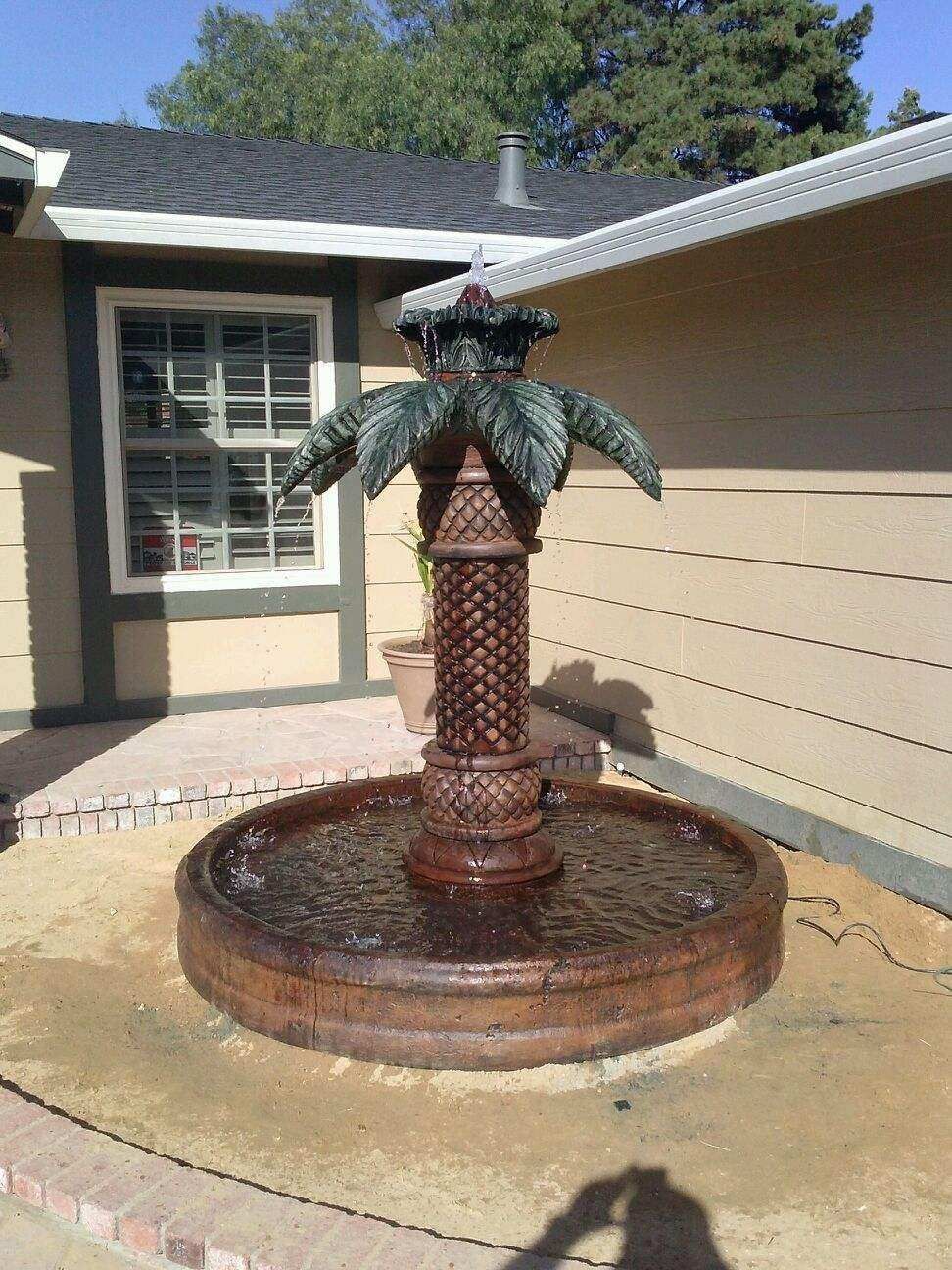 Decorative bronze fountain shaped like a palm tree in a courtyard beside a house