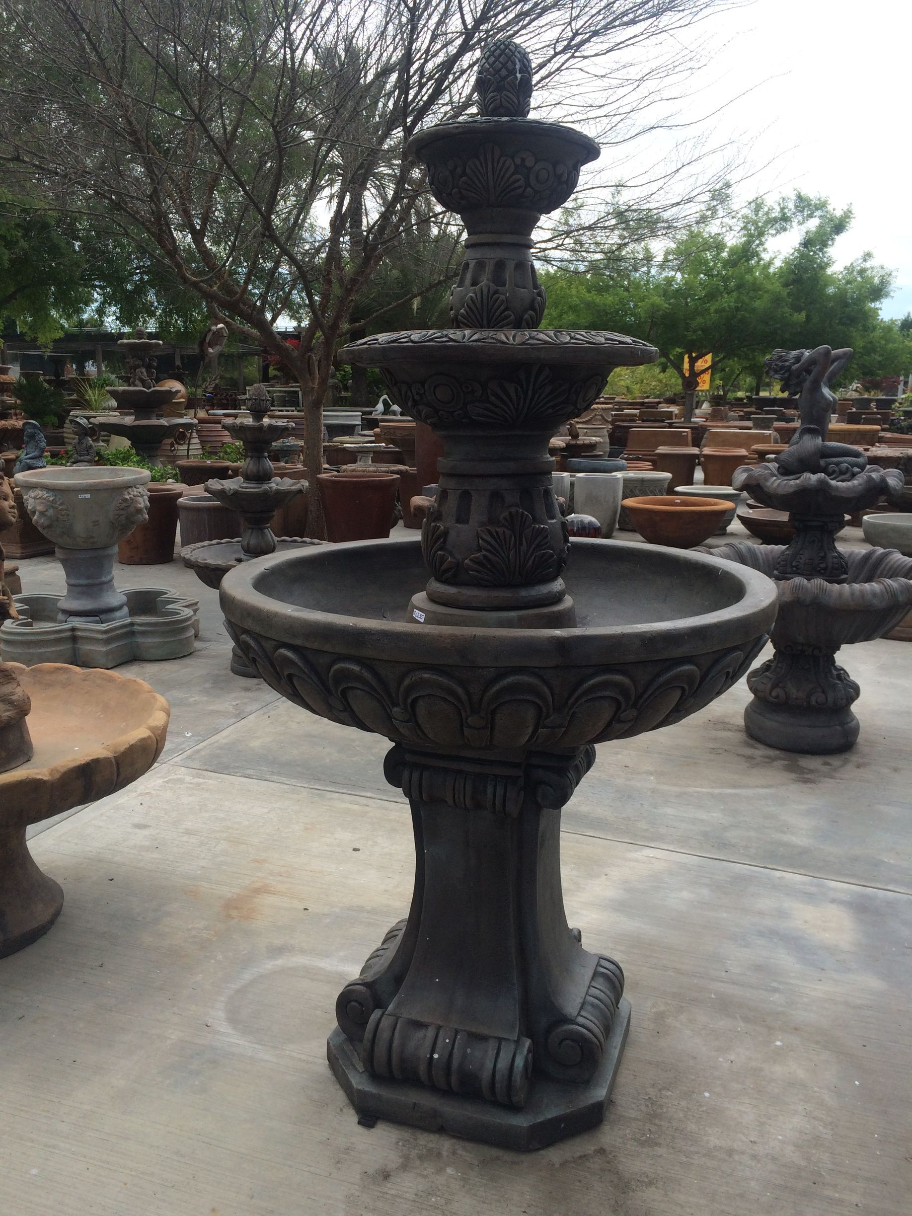 Ornate black stone fountain in an outdoor garden display area, surrounded by other fountains and trees
