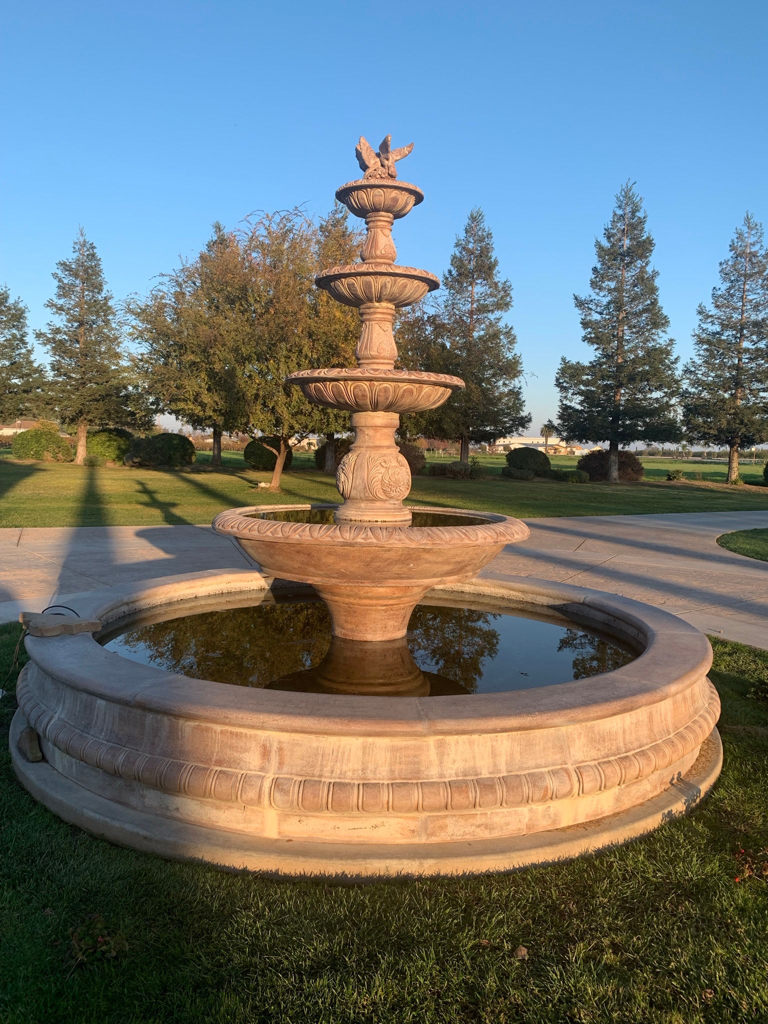 Tiered stone fountain in a park, with water basin and trees at sunset