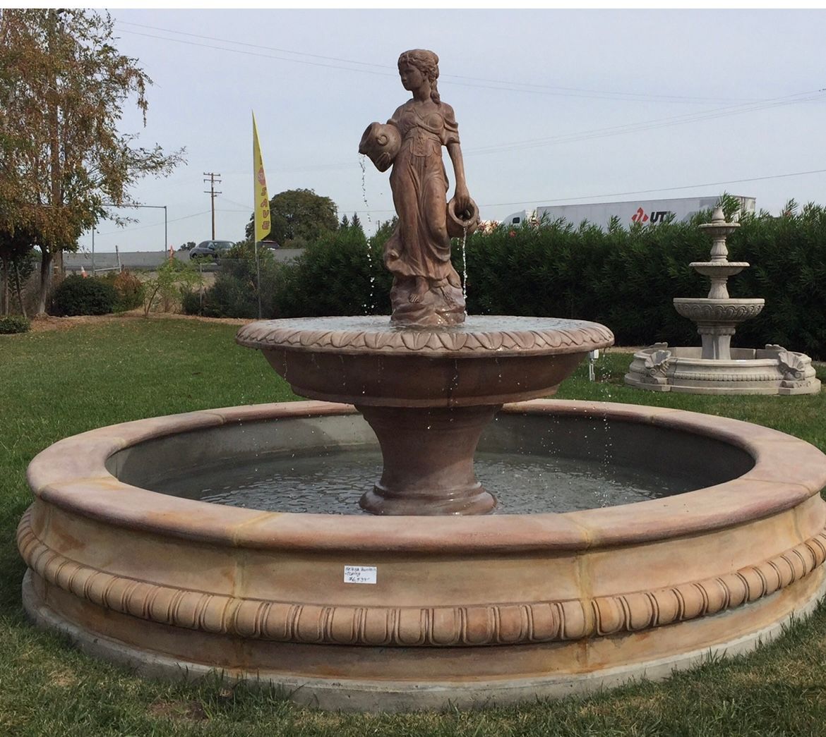 Stone fountain with a central statue in a grassy garden, with a smaller fountain to the right.