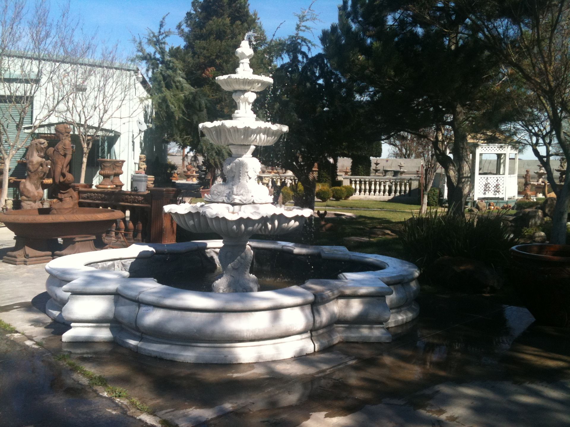 White tiered fountain in a garden courtyard with trees and benches
