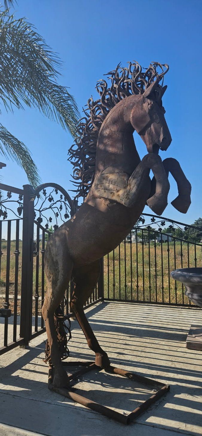 Bronze horse statue rearing on a pedestal behind a black wrought-iron gate in bright sunlight