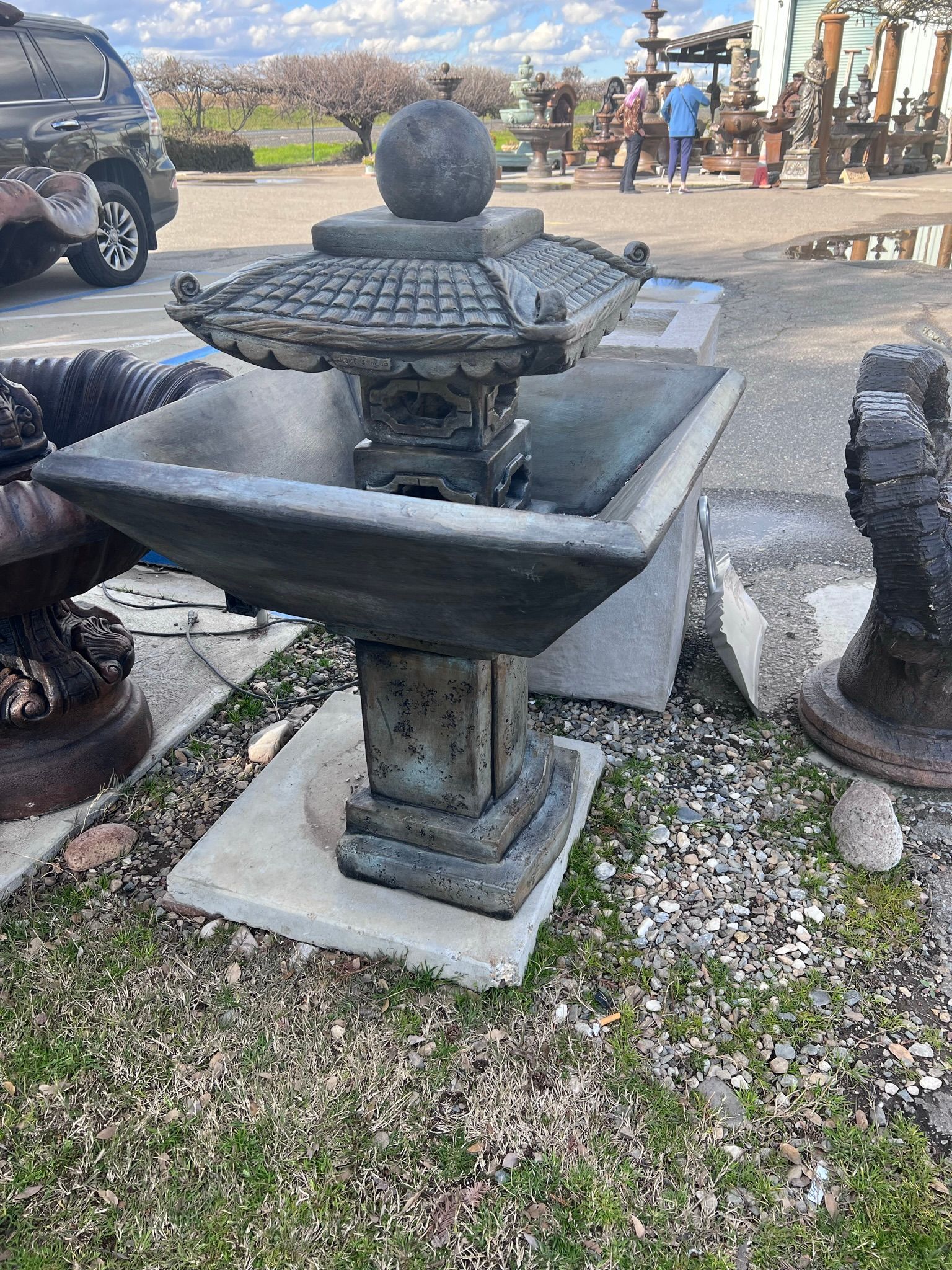 Stone garden fountain with tiered basin and round finial on a concrete pad outdoors