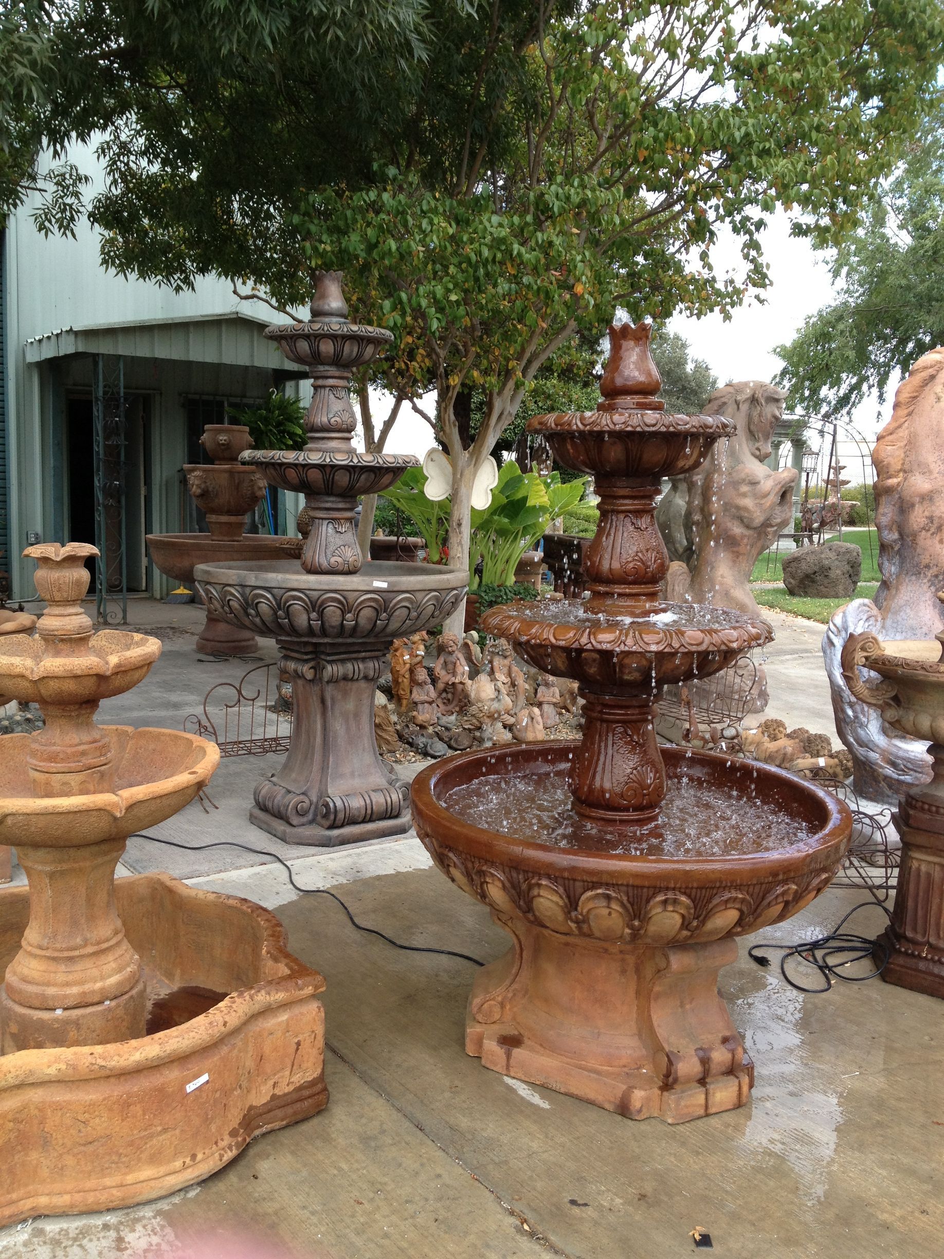 Tiered stone and concrete garden fountains in tan, gray, and rust colors on a wet patio.