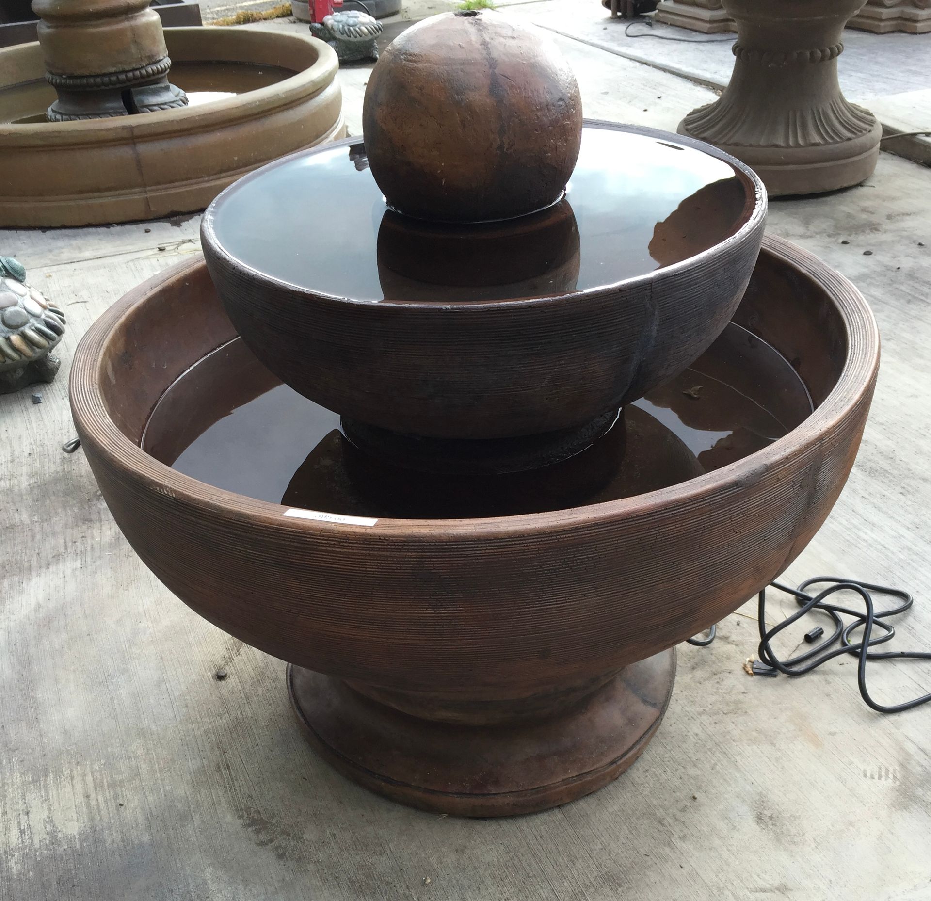 Rust-colored tiered outdoor fountain with a spherical top, standing on a concrete surface.