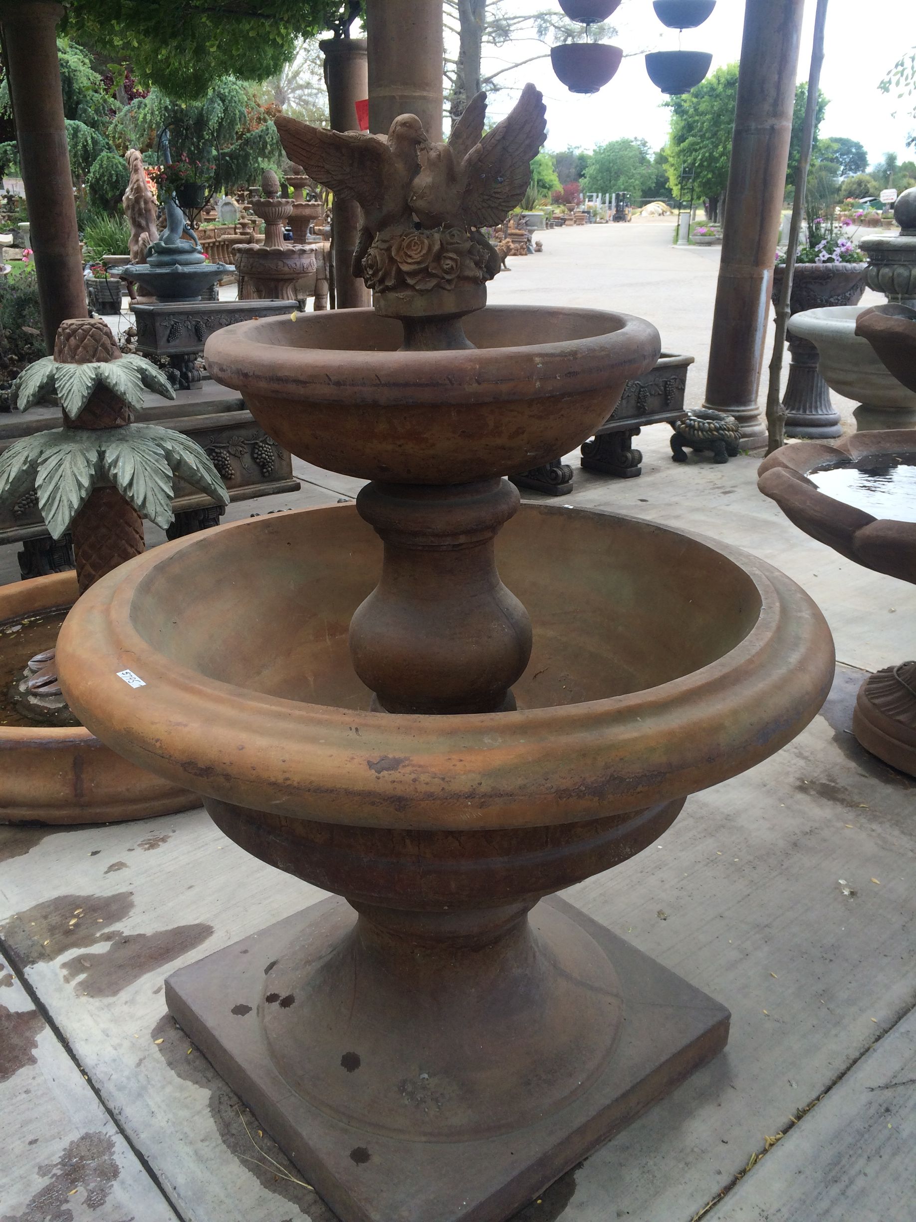 Rustic terracotta tiered fountain with decorative bird sculpture in a garden display area