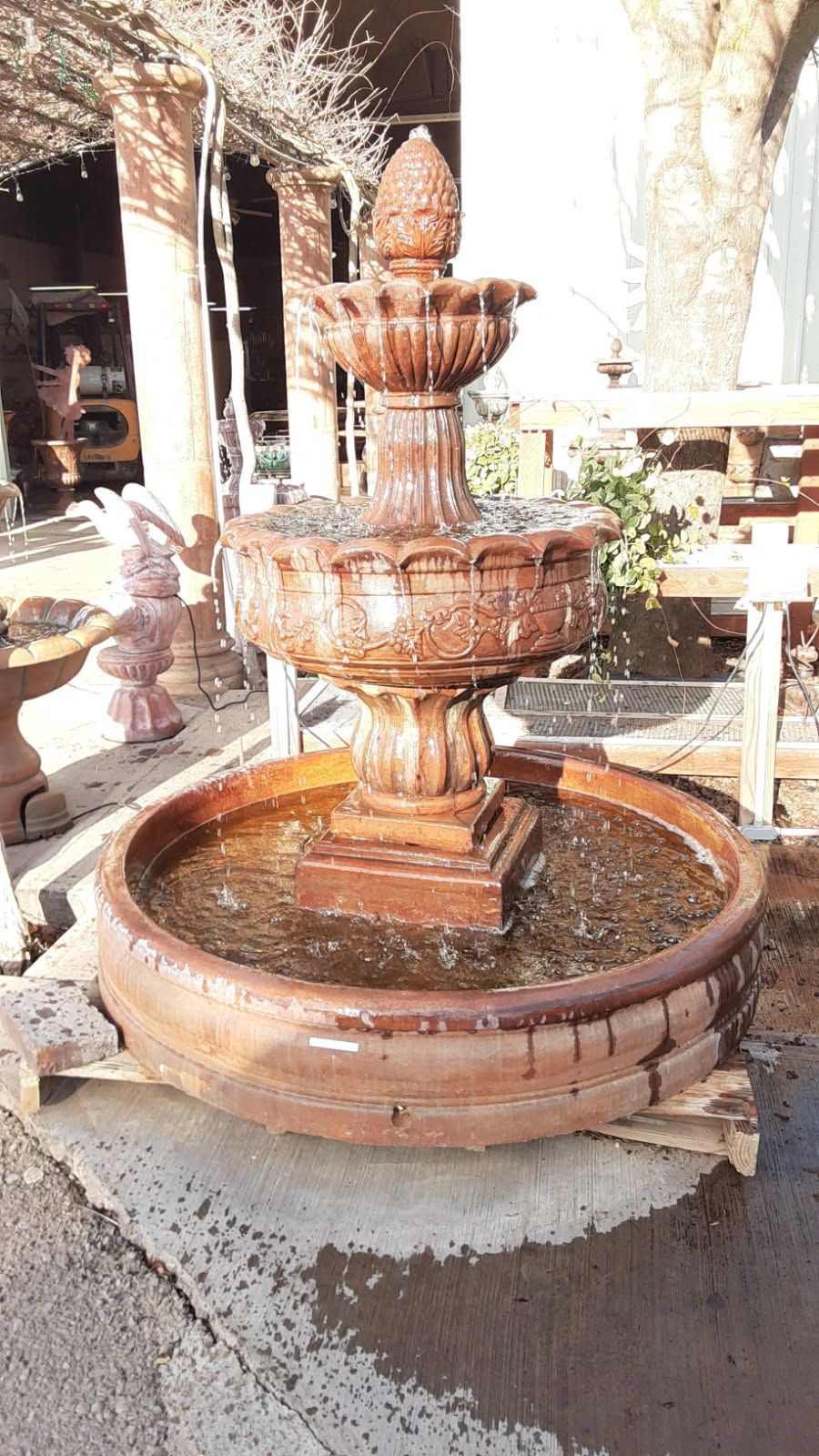 Small terracotta fountain with water in a round basin outdoors under bright sunlight