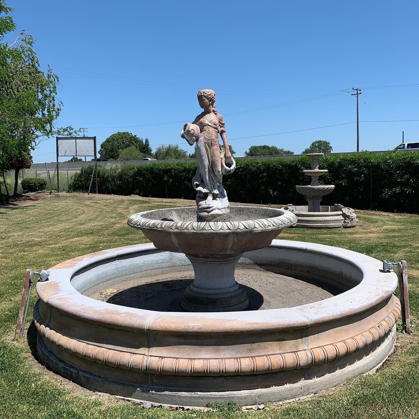 Stone fountain with a cherub statue in a grassy park under a clear blue sky
