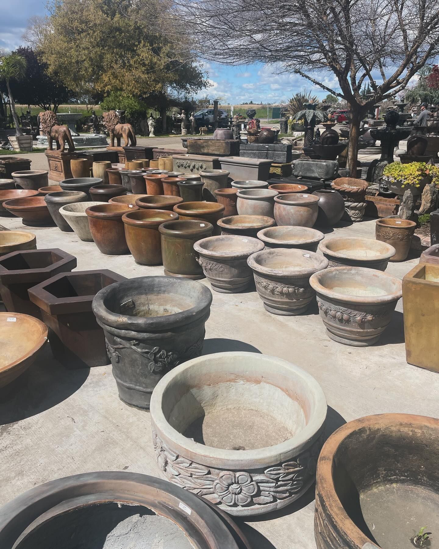 Outdoor market display of many large decorative pots and planters under a bright sky