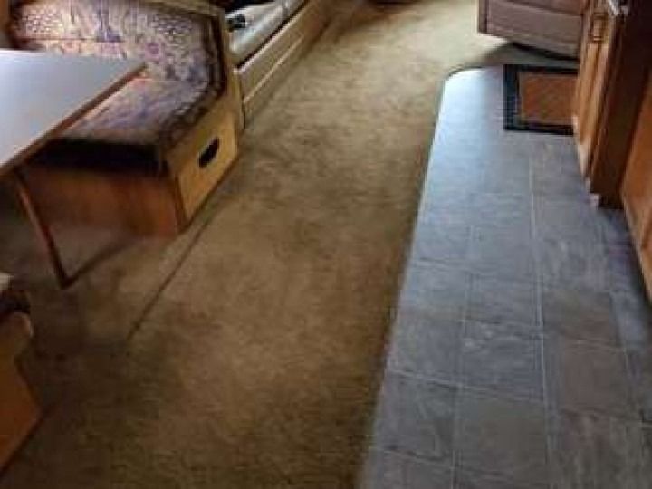 Interior of RV with carpeted and tiled flooring, table, and seating.