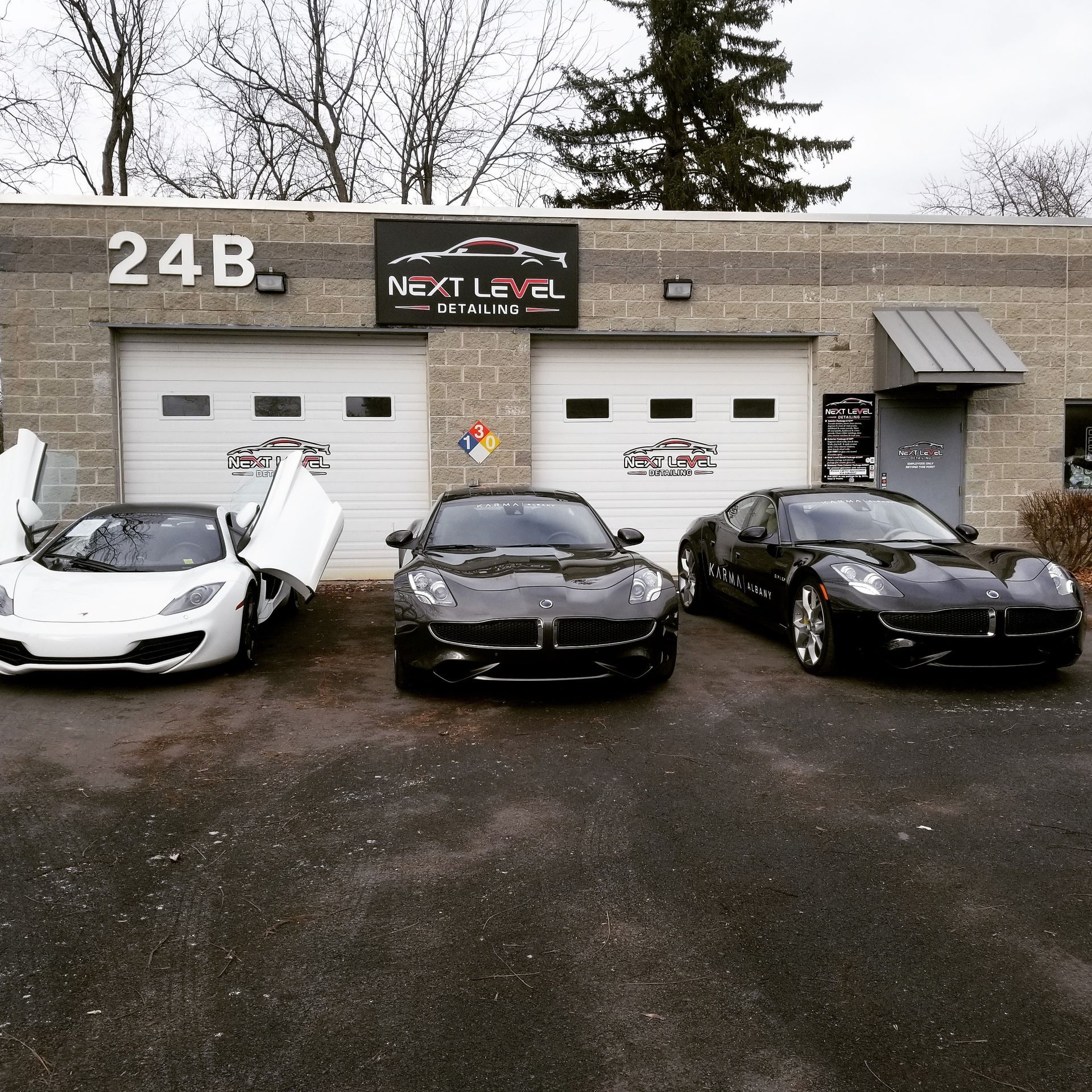 Three luxury cars in front of a car detailing business with a grey exterior.