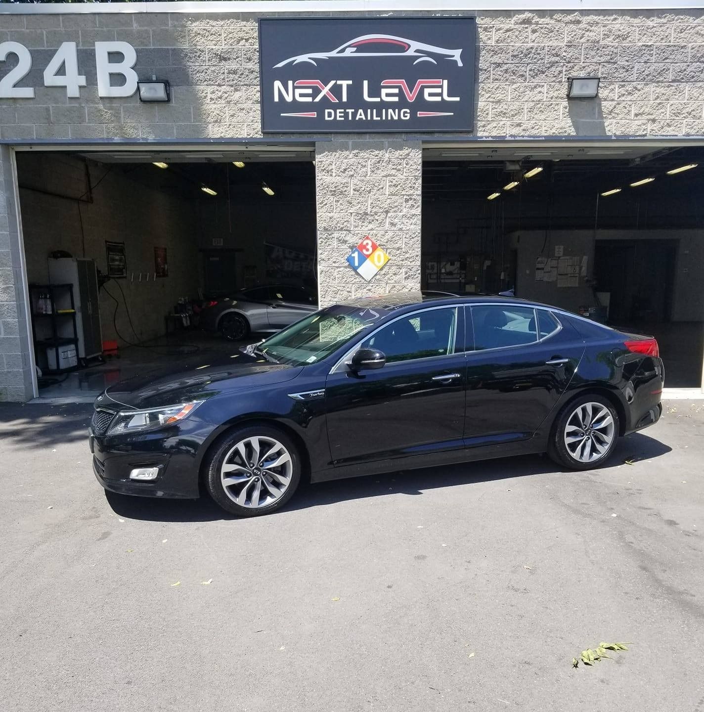 Black Kia Optima parked in front of Next Level Detailing shop.