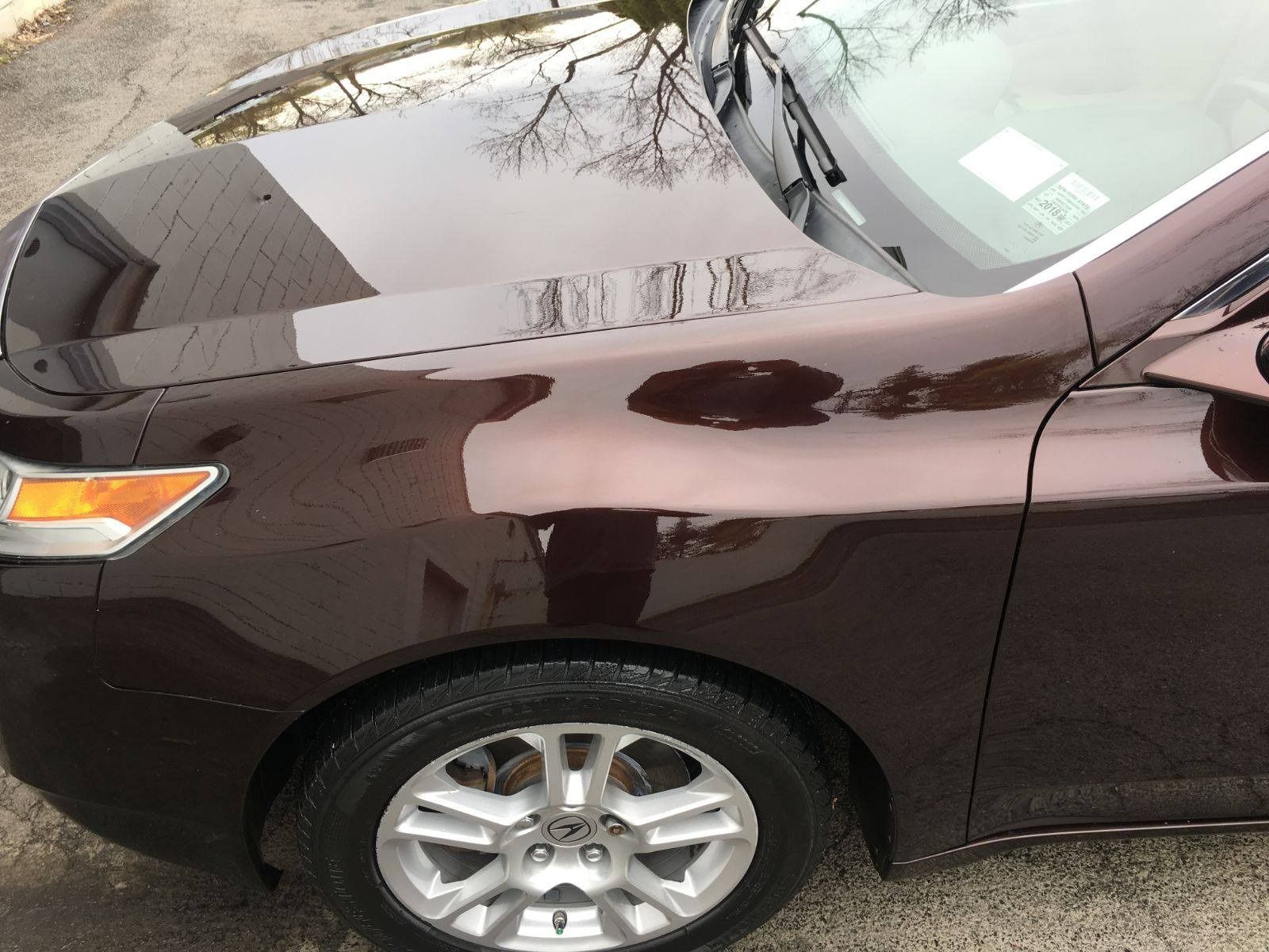Dark red car, hood and front fender reflecting trees, parked on asphalt.