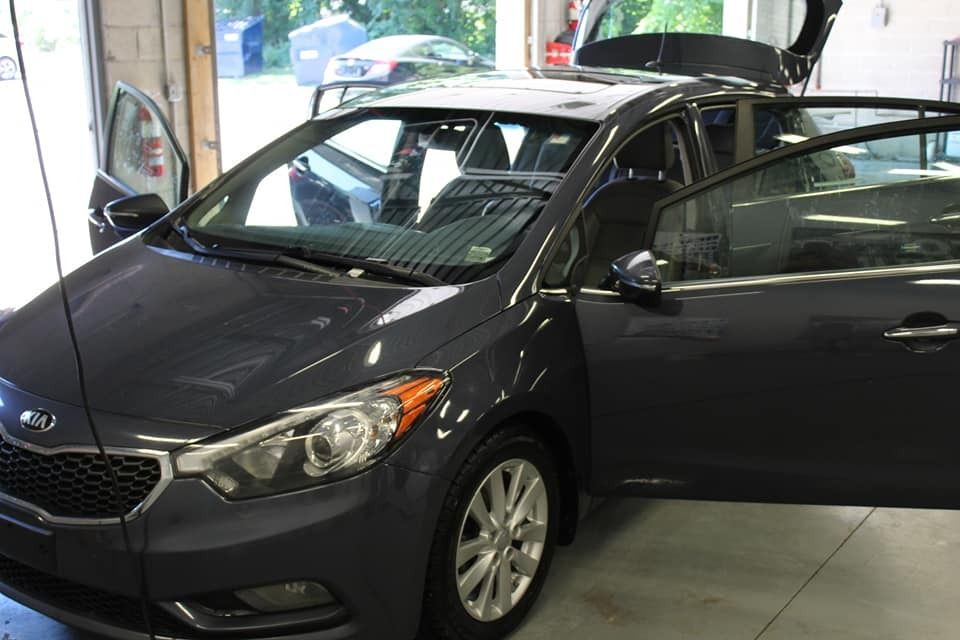 Dark gray Kia Forte with doors open, parked in a garage.