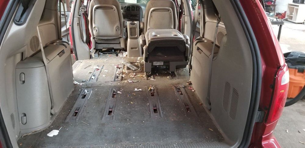 Interior of a red minivan with seats removed, debris on the floor, and an orange vacuum.