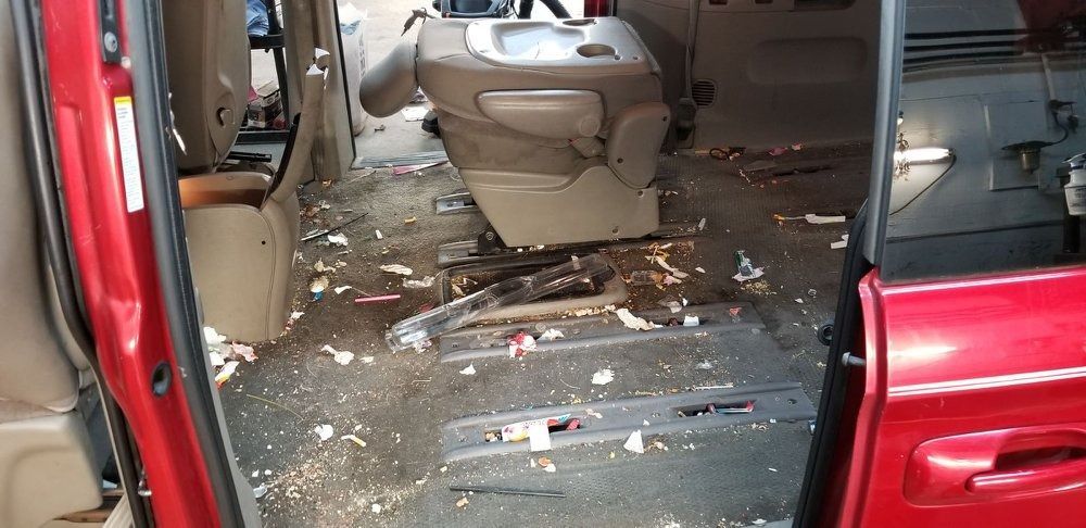Interior of a van with red trim and a removed seat. The floor is covered in debris.