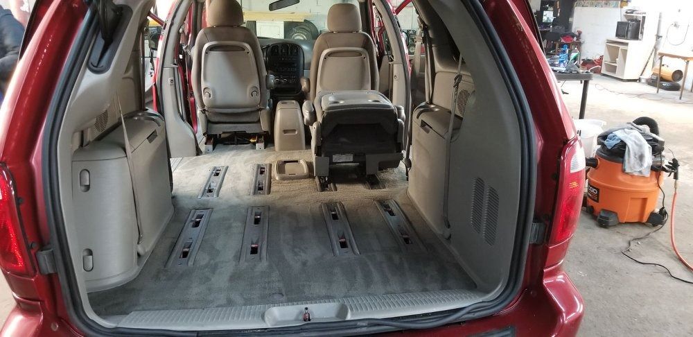 Red minivan interior with seats removed, revealing gray floor. A vacuum cleaner is in the background.