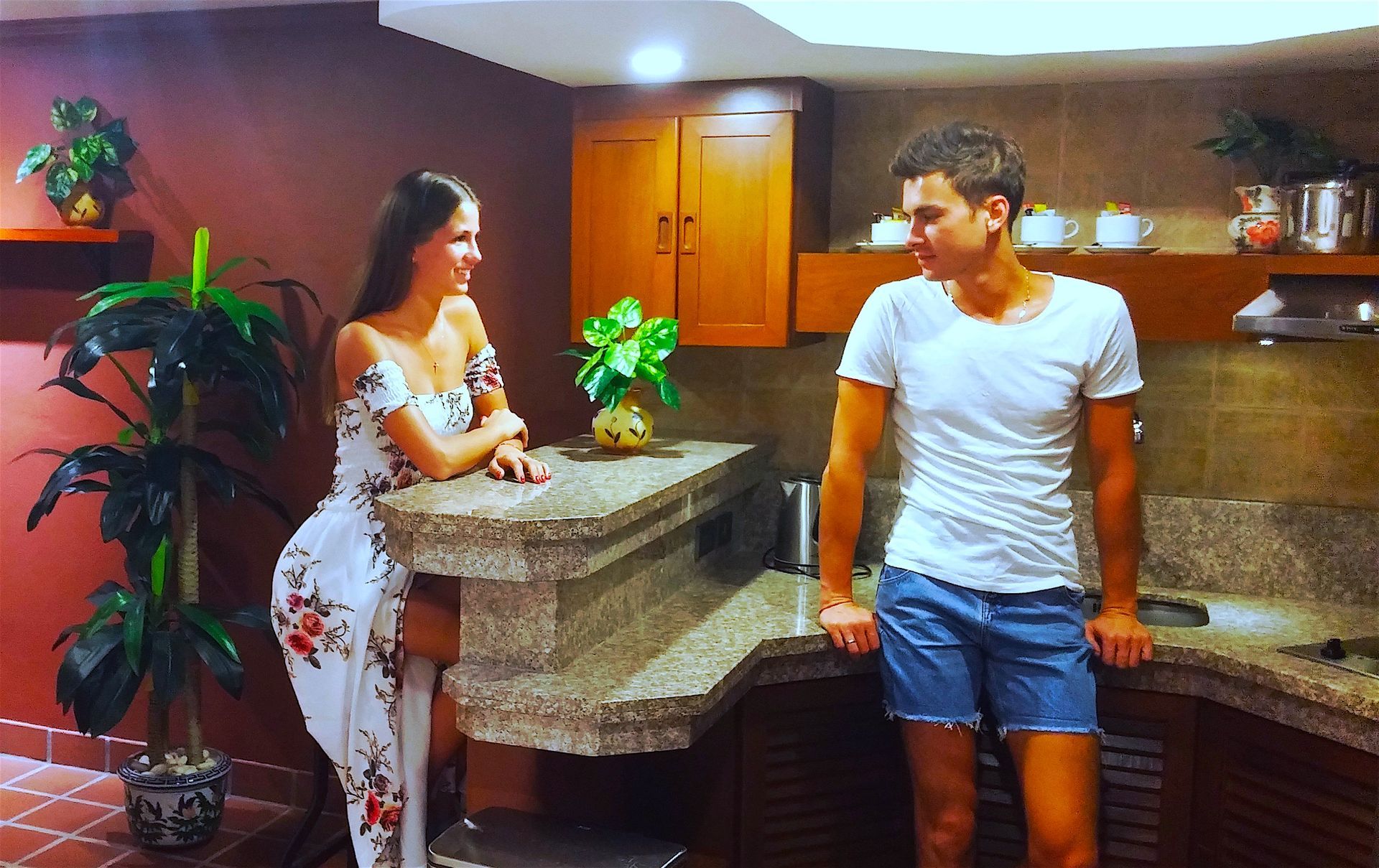 A man and a woman are standing in a kitchen talking to each other.