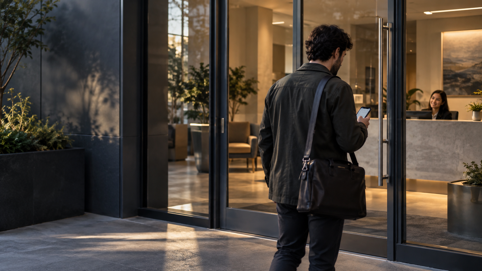 Person standing outside a modern glass-front building, looking at a lit reception desk inside.