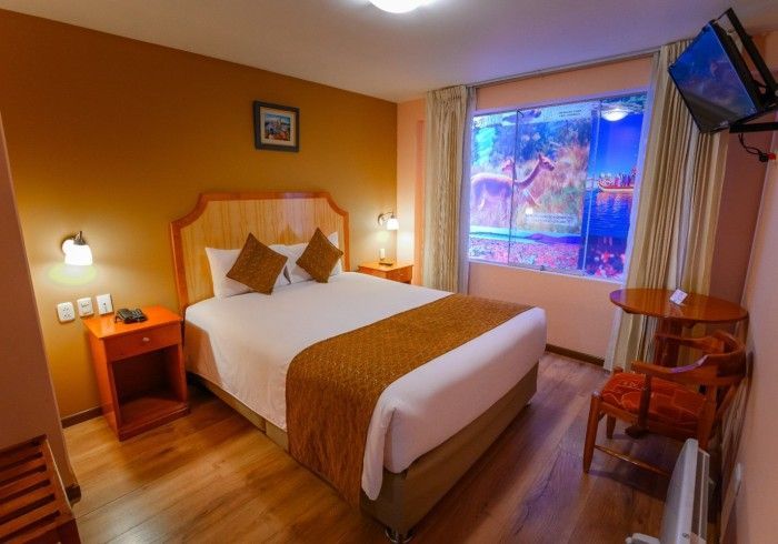 Una habitación de hotel con una cama de matrimonio, muebles de madera, una pequeña mesa de comedor con una silla.