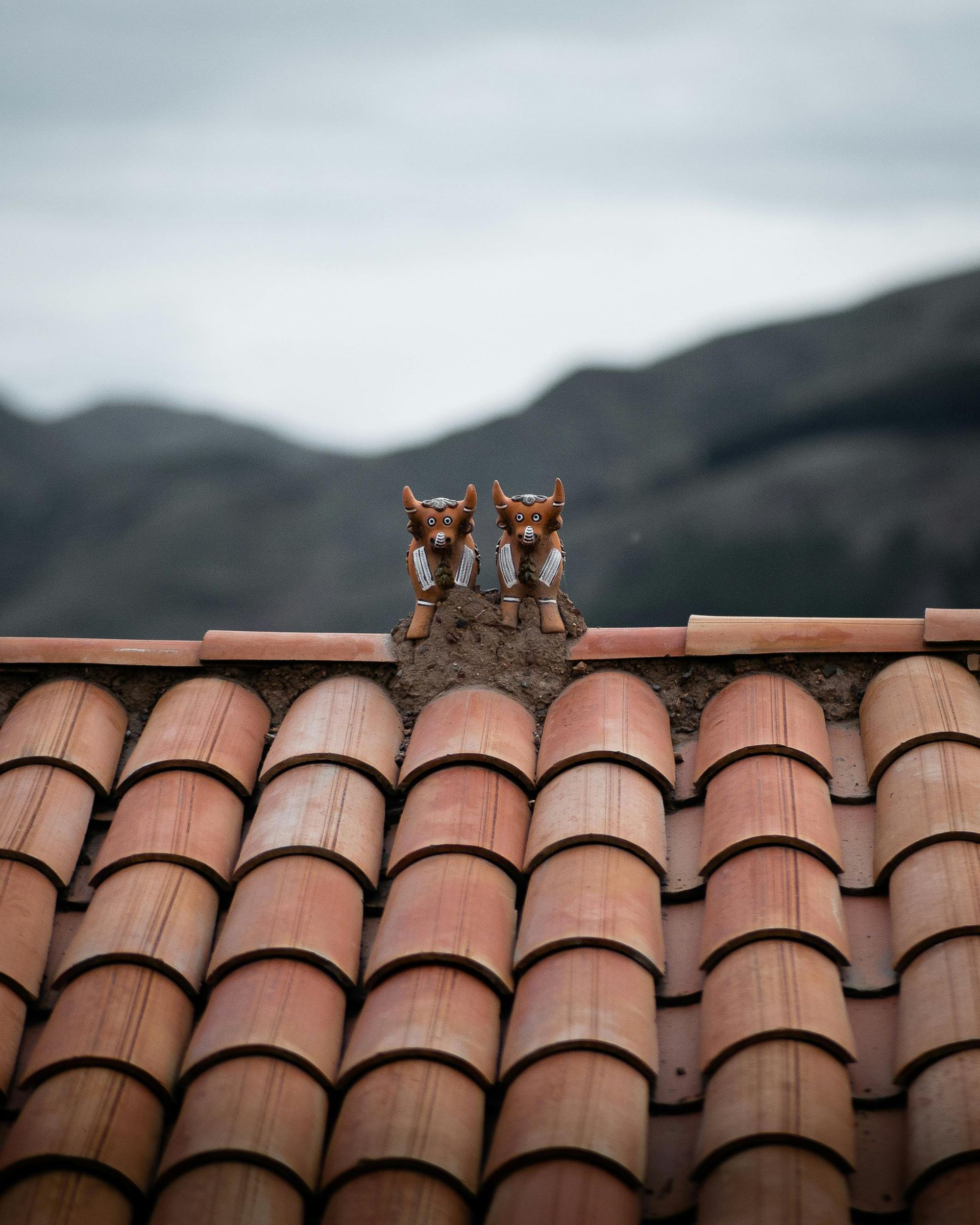Dos pequeñas figuritas de animales de cerámica marrón se encuentran sobre la cumbrera de un tejado de tejas de terracota.