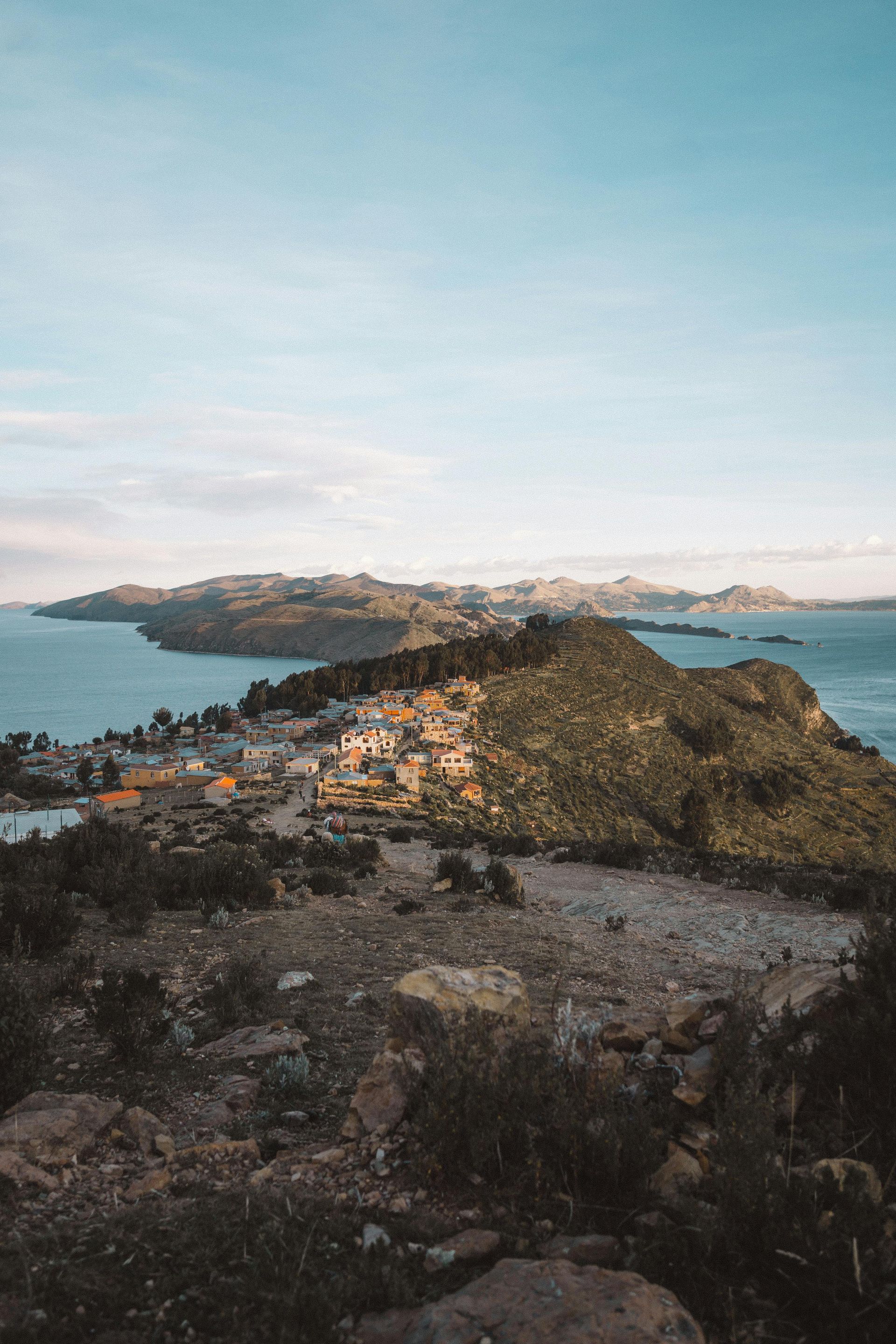 Un pequeño pueblo se asienta sobre una cresta rocosa con vistas a un vasto lago bajo un cielo azul claro y despejado.