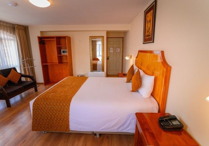 Una habitación de hotel con una cama grande, cabecero de madera, dos almohadas, un sofá marrón y un armario abierto.