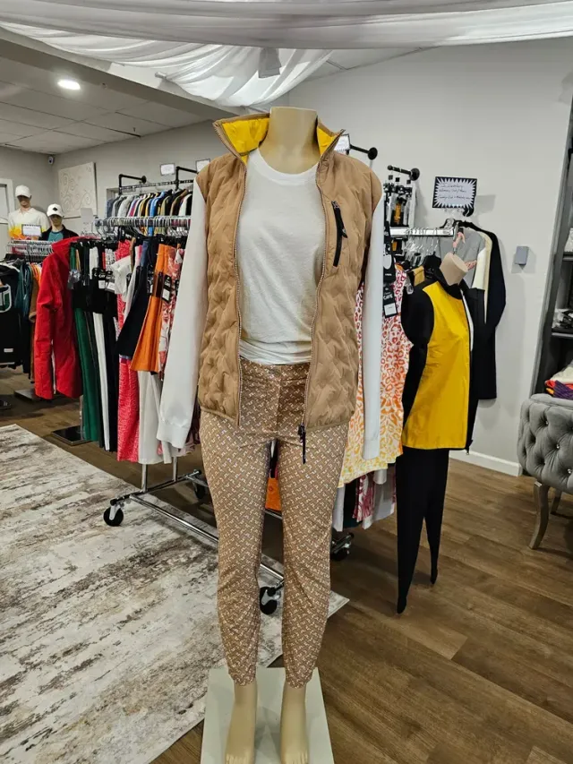 Mannequin wearing tan jacket, white top, patterned pants, and pink heels in a clothing store.