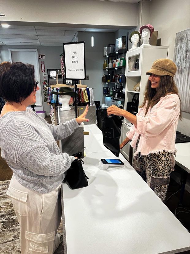 Two people chatting across a store counter, one handing over a black item.