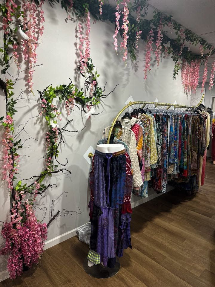 Boutique clothing rack under hanging pink floral decor, with colorful dresses and a mannequin dress display