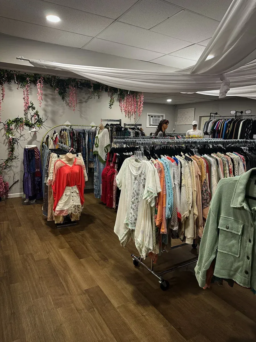 Clothing boutique with racks of dresses and tops under hanging floral décor on a wood floor.